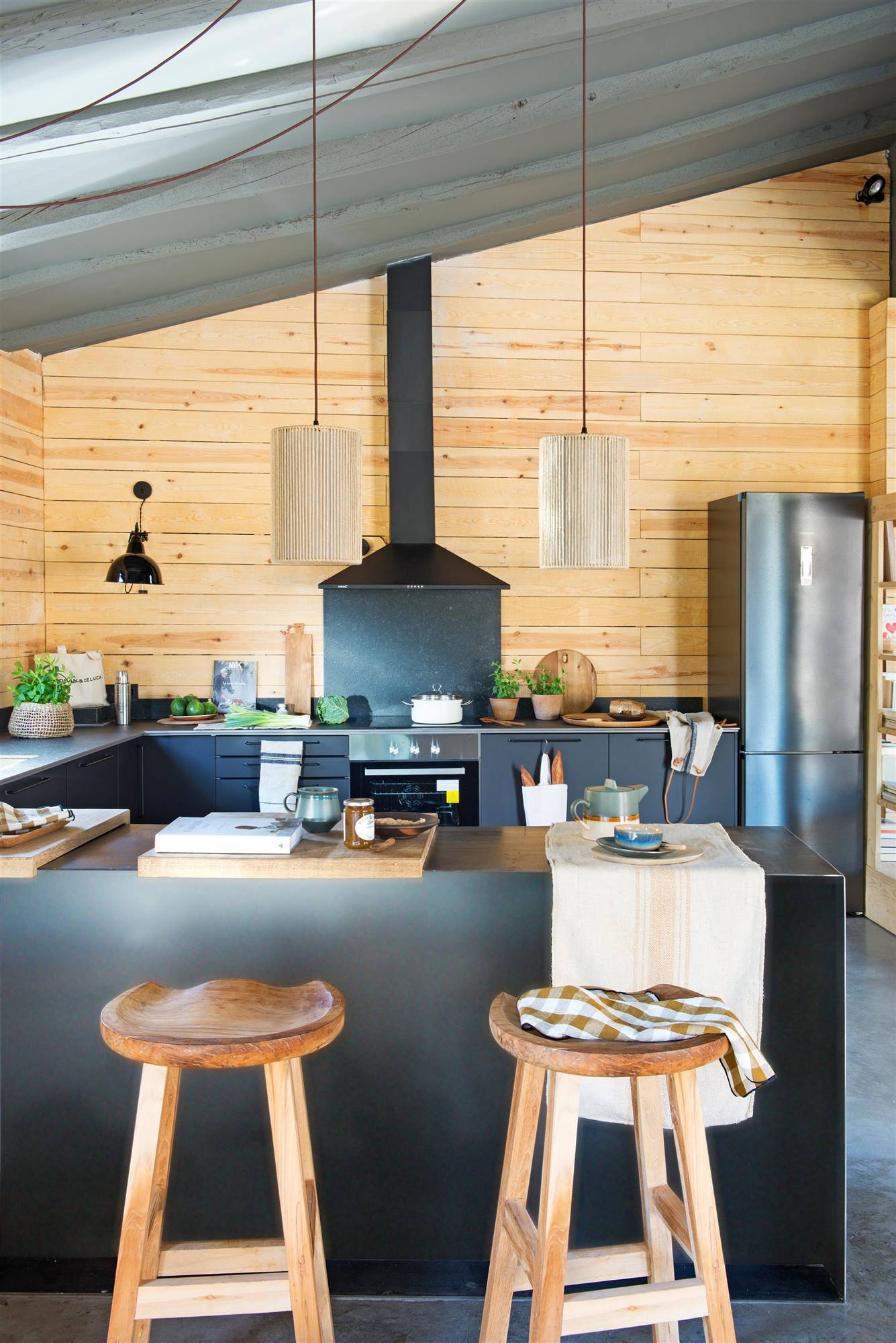 Una cocina negra con revestimiento de madera, vigas en el techo y campana extractora. 