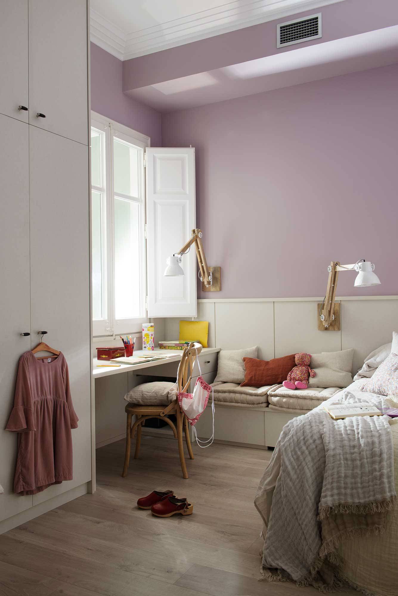 Dormitorio infantil en blanco y lila, escritorio y banco con cojines.
