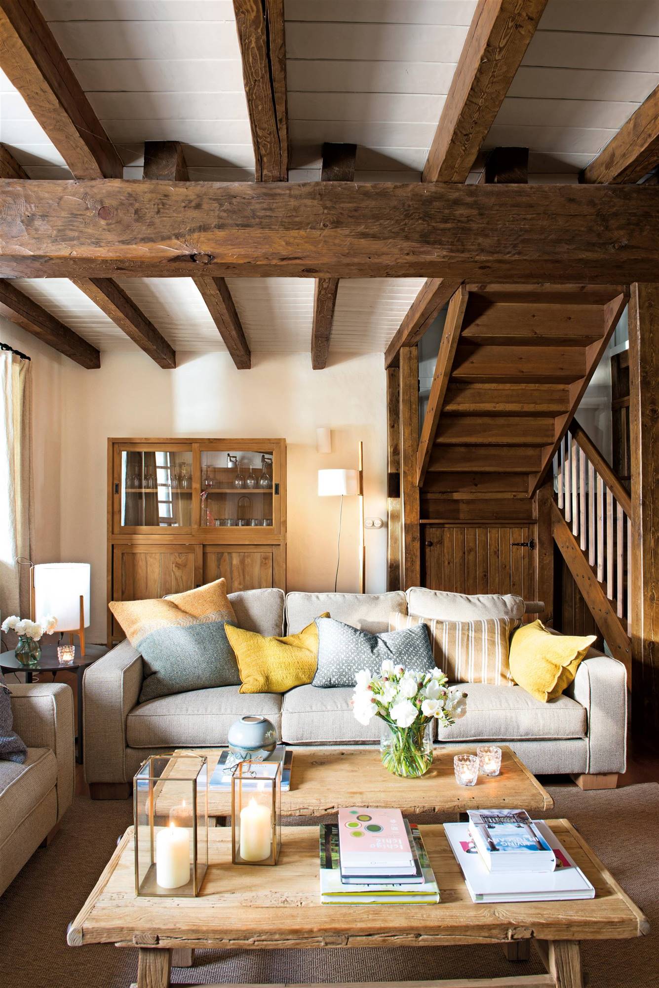 Salón con vigas y escaleras de madera y sofá gris.  