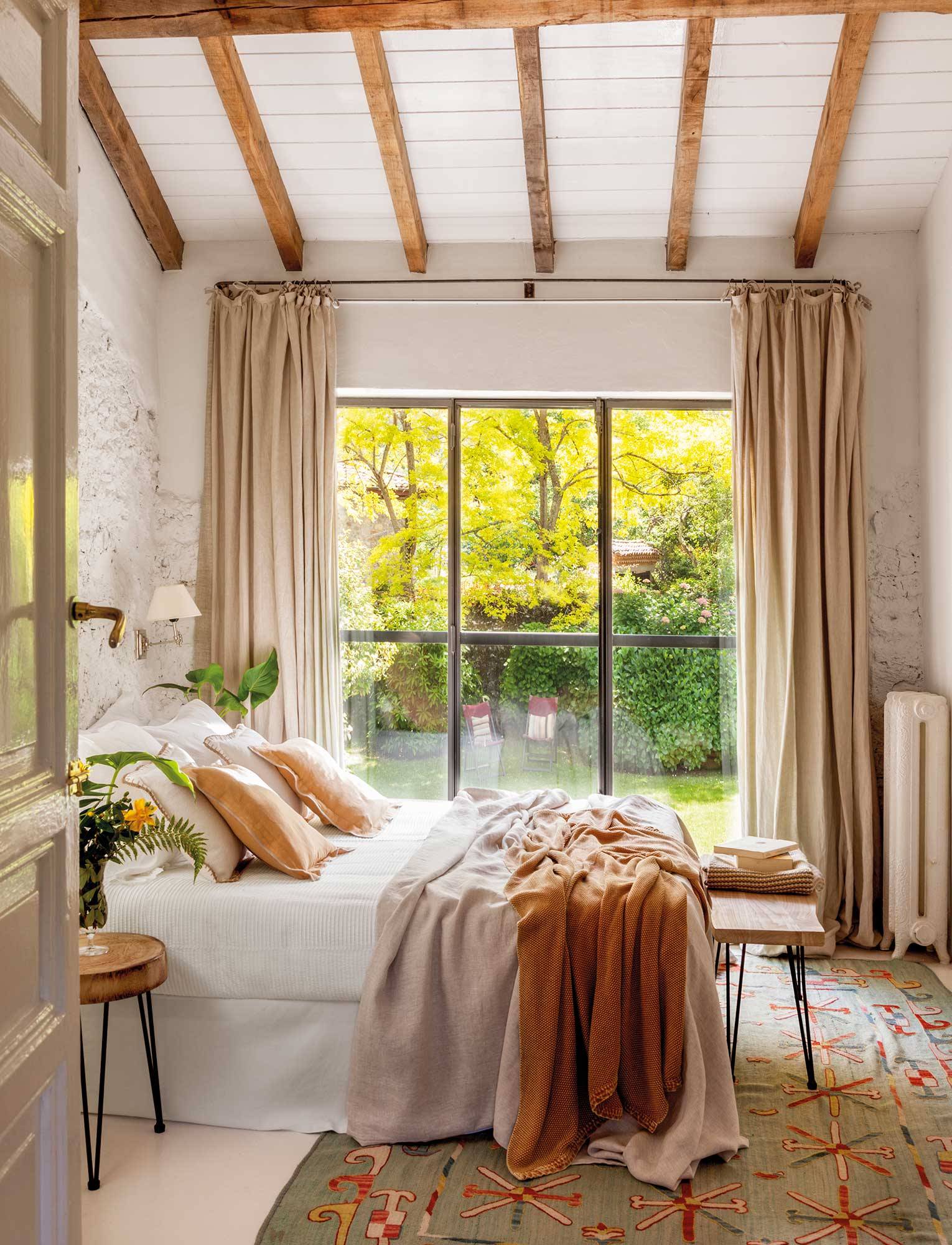 Dormitorio de casa rústica con paredes de piedra blanqueadas y gran ventanal con vistas al jardín 00510584