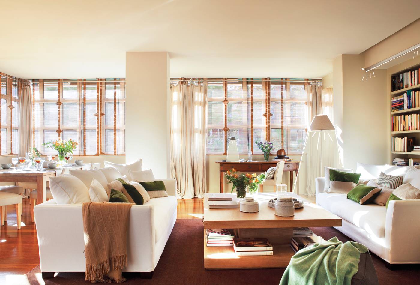 Salón con sofás blancos, muebles de madera y pared con ventanales.
