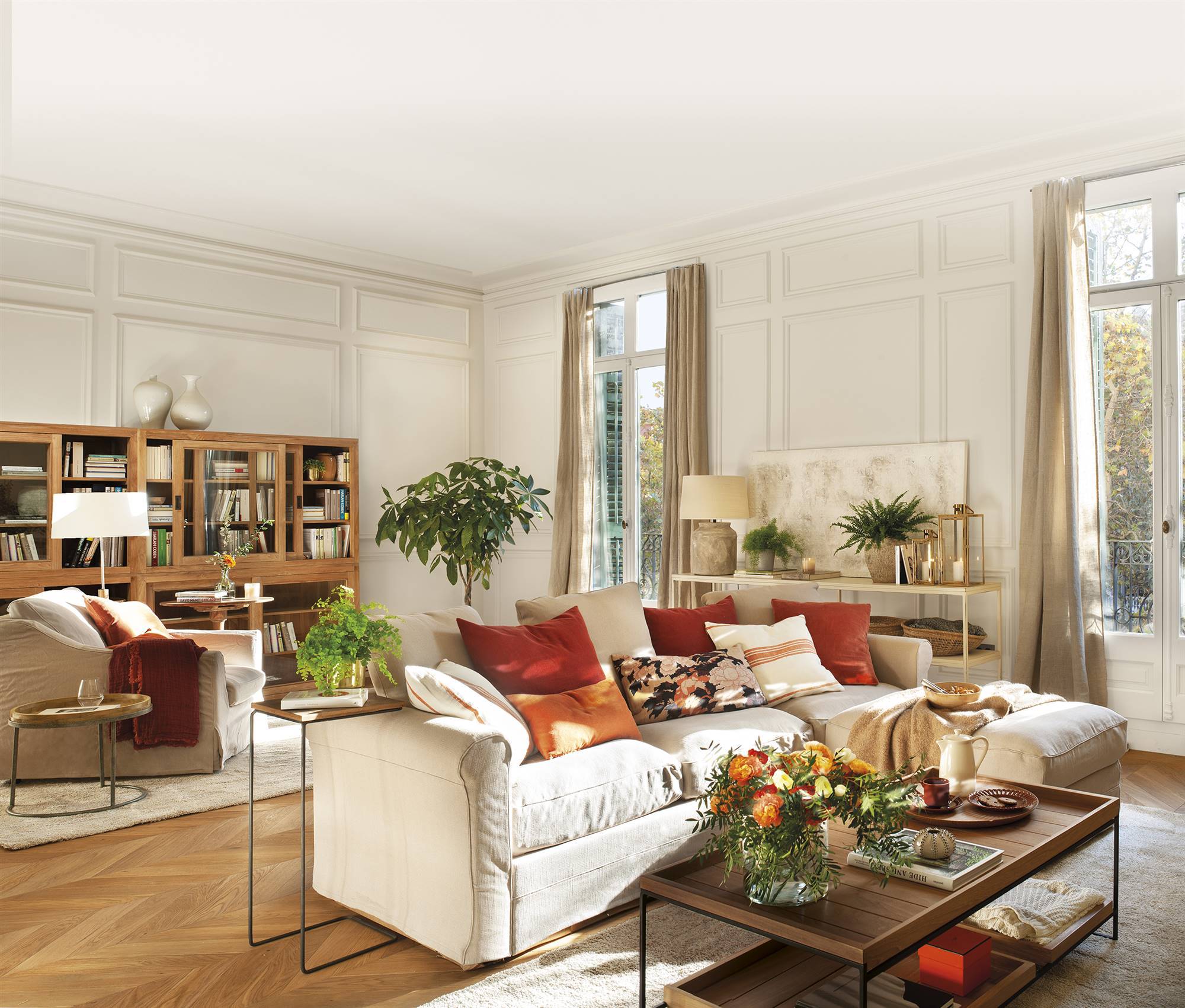 Salón con molduras en las paredes, sofás de color beige y muebles de madera. 