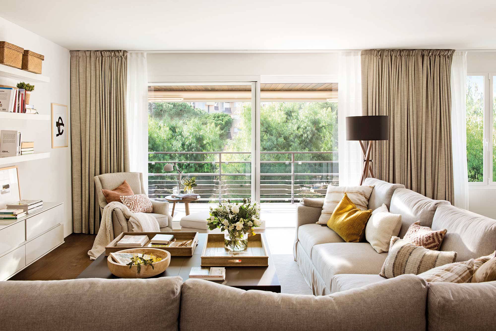 Salón moderno con ventanal a la terraza, sofás beige y cortinas dobles.  