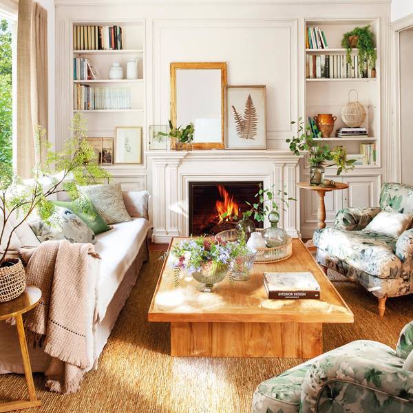 Salón con sofá beige y butaca con estampado floral, chimenea y mesa de centro de madera. 