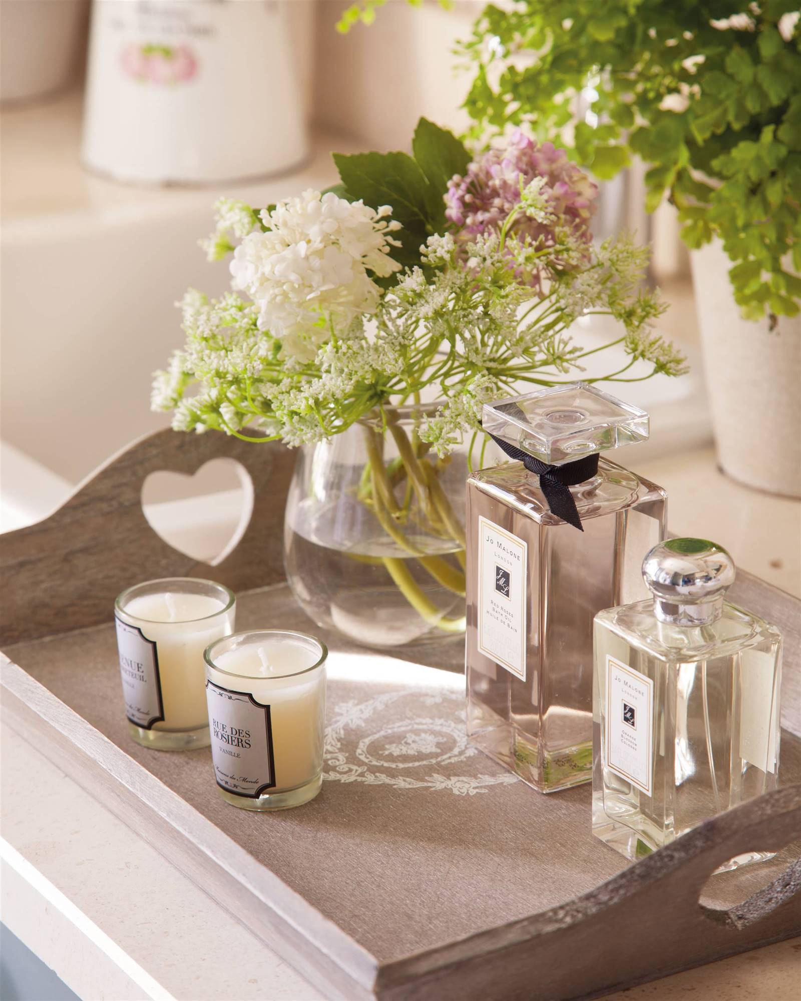 Perfumes, velas y un jarrón con flores sobre una bandeja en el baño