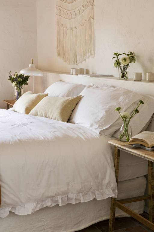 Dormitorio de primavera en blanco total con decoración de croché en pared de cabecero. 