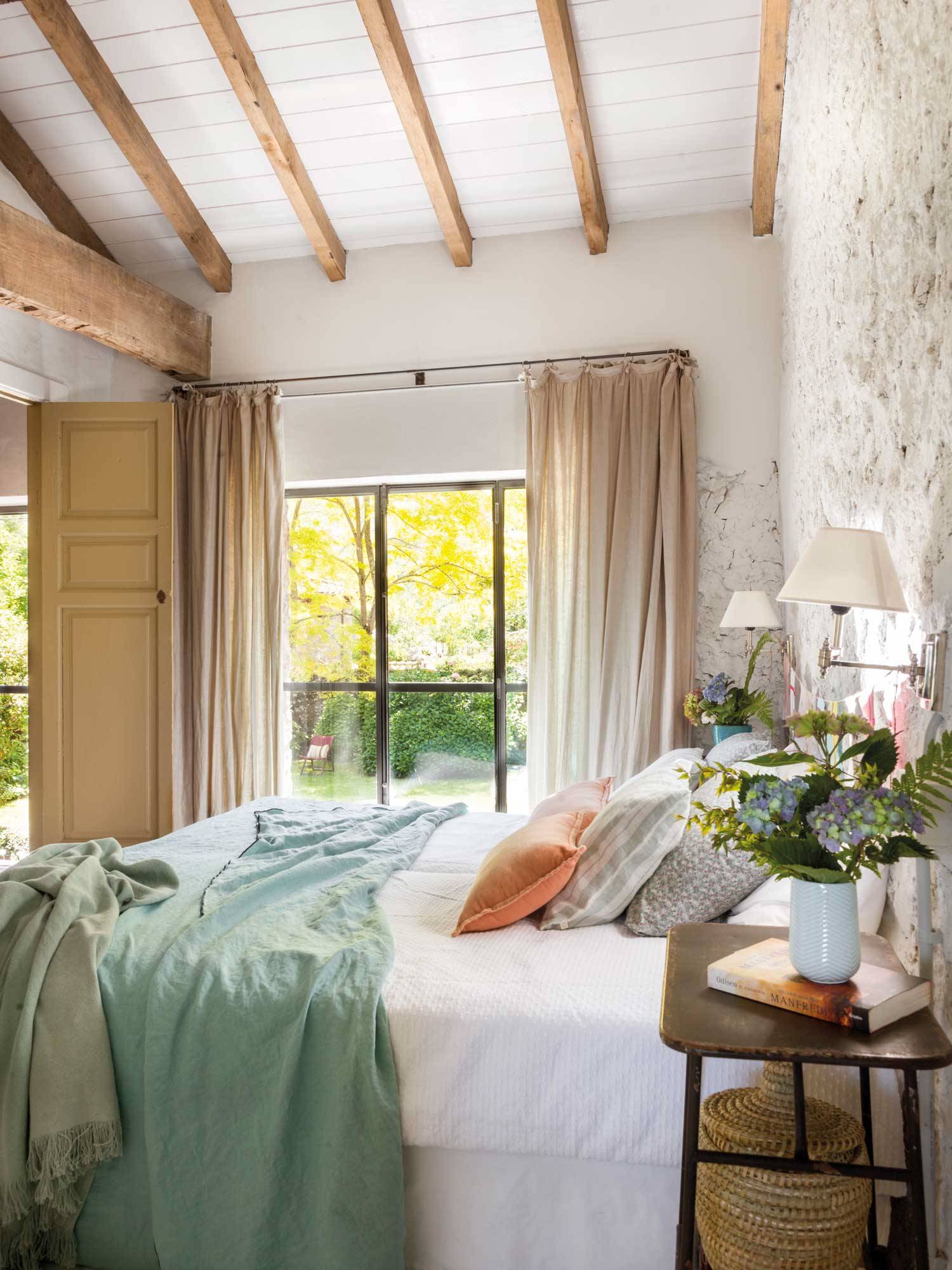 Dormitorio de primavera con pared encalada y vigas de madera en el techo.