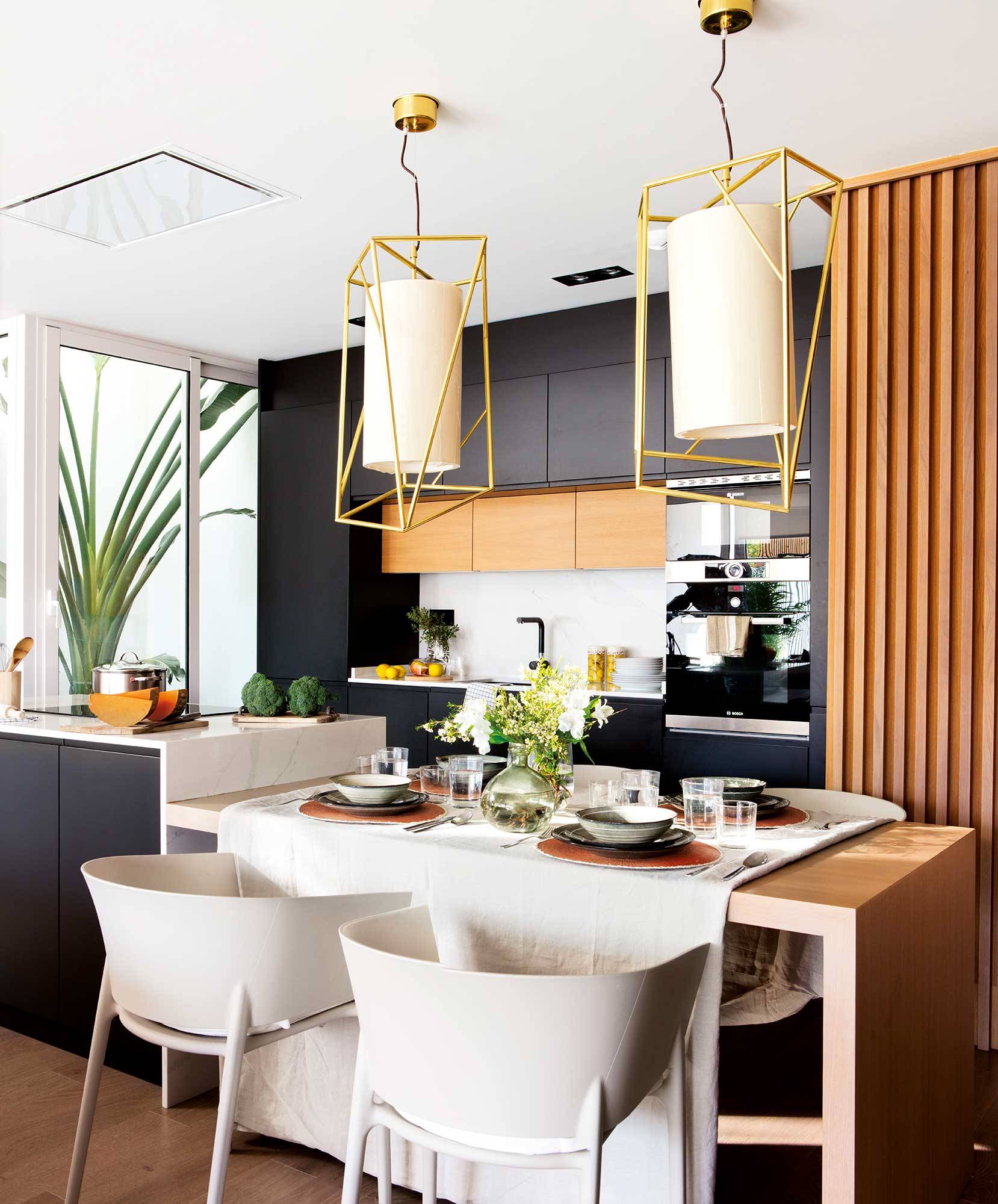 Moderna cocina en negro, lámparas de diseño y barra con sillas que hace de office. 
