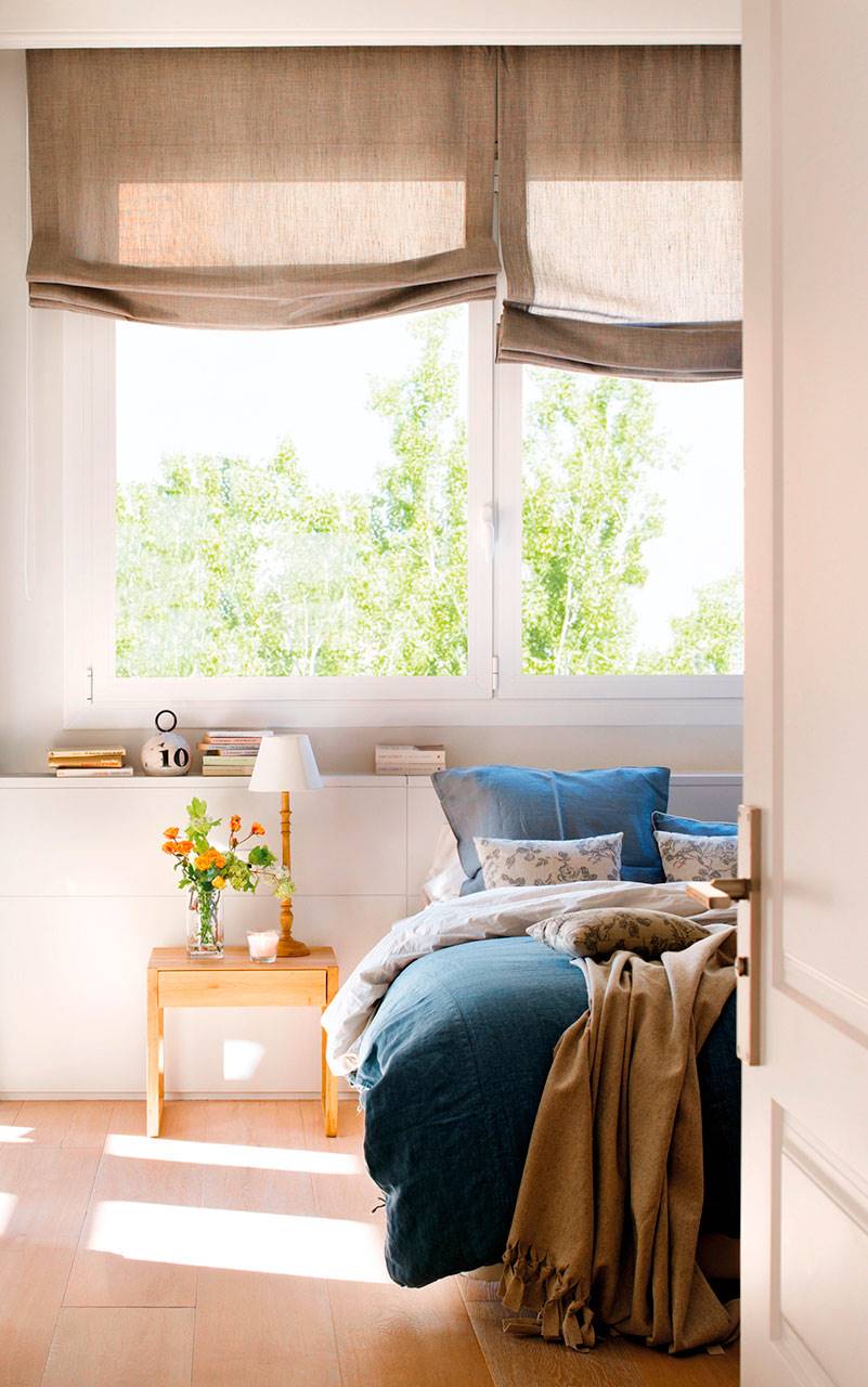 Dormitorio en blanco con cabecero a medida bajo la ventana y textiles en azul