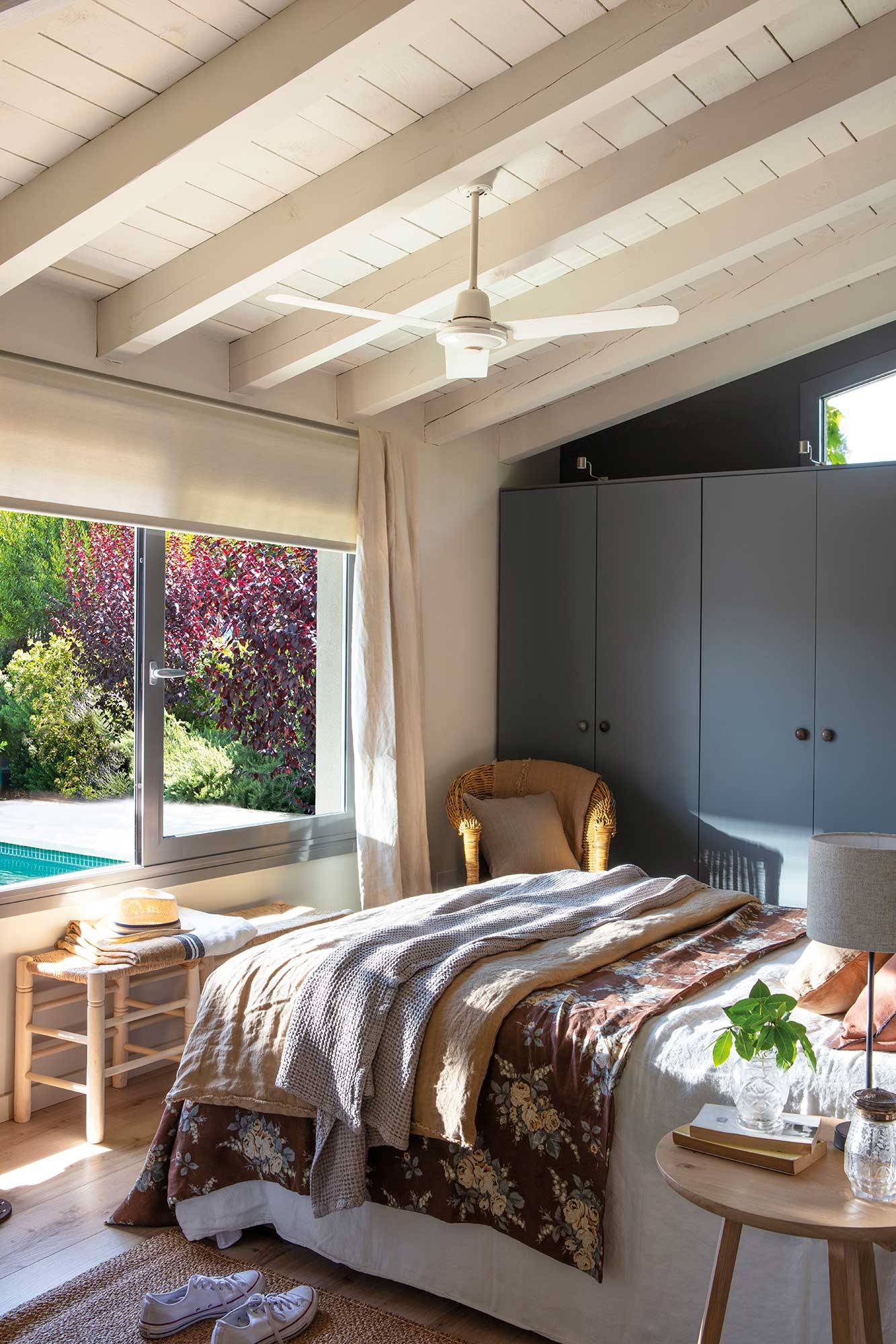 Dormitorio con vigas, gran ventanal con vistas al jardín y pared de armarios gris