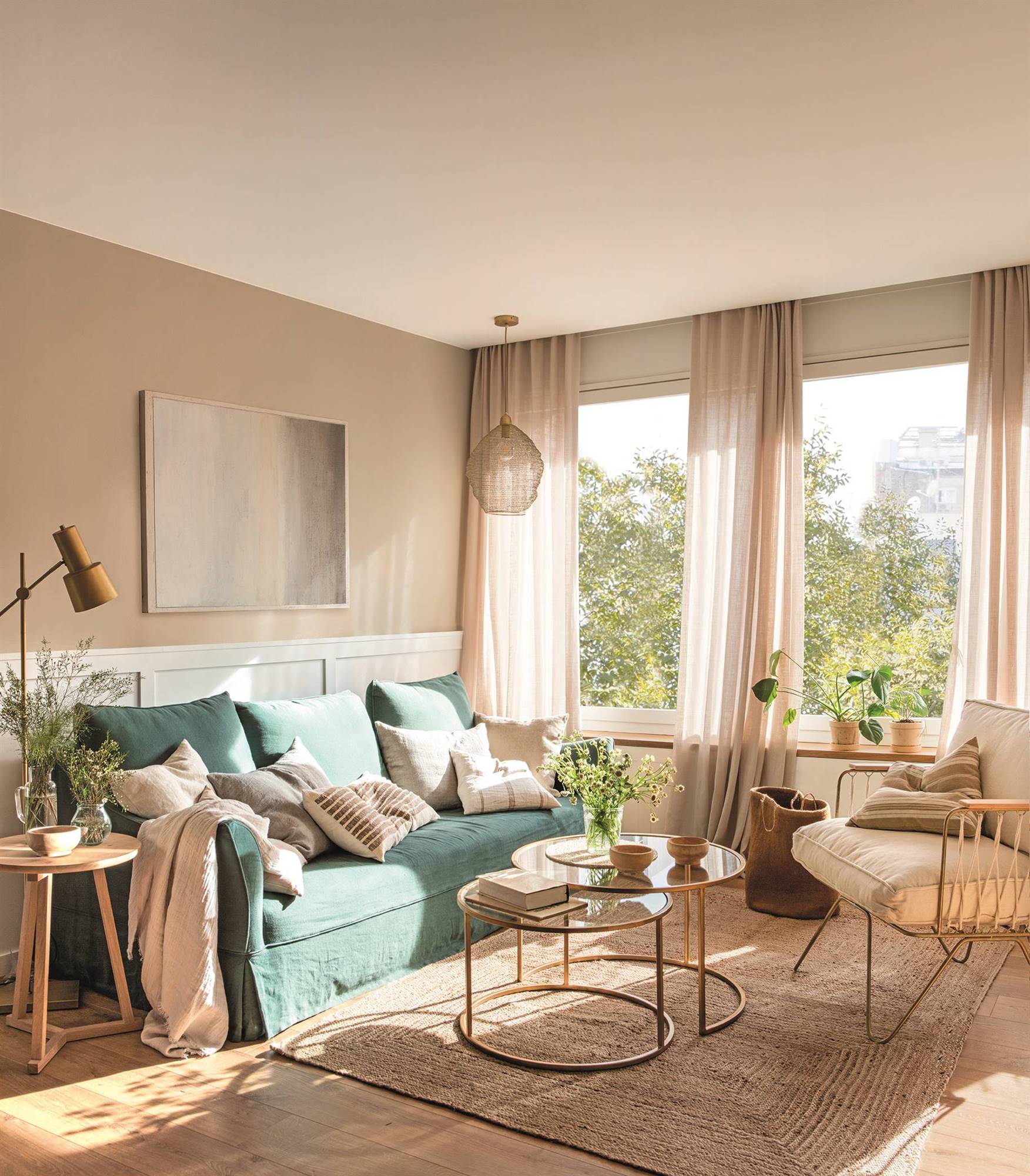 Salón con sofá verde, pared con arrimadero y mesas de centro redondas con acabado dorado. 