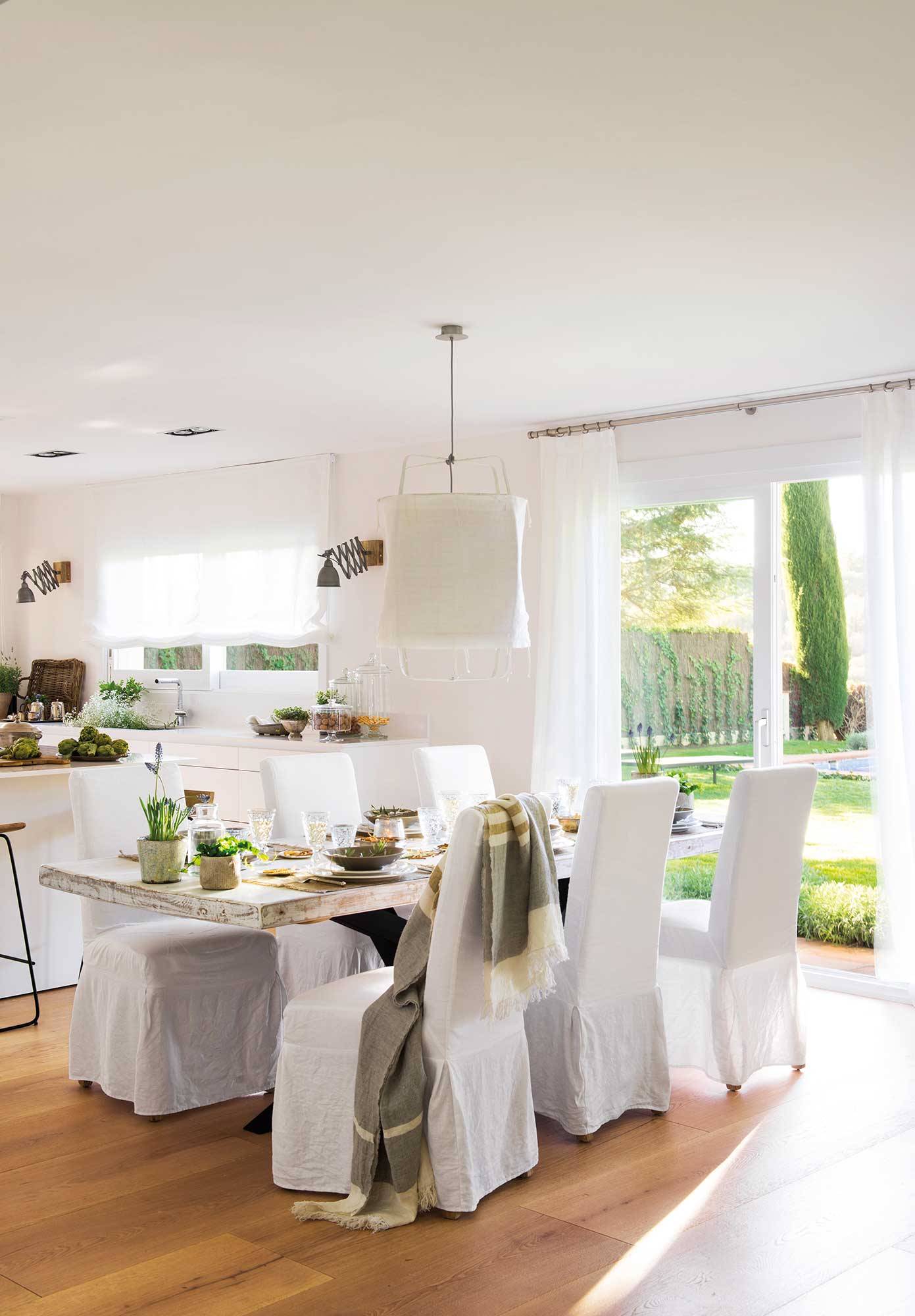 Comedor abierto a la cocina con sillas con fundas de lino blancas 00480348