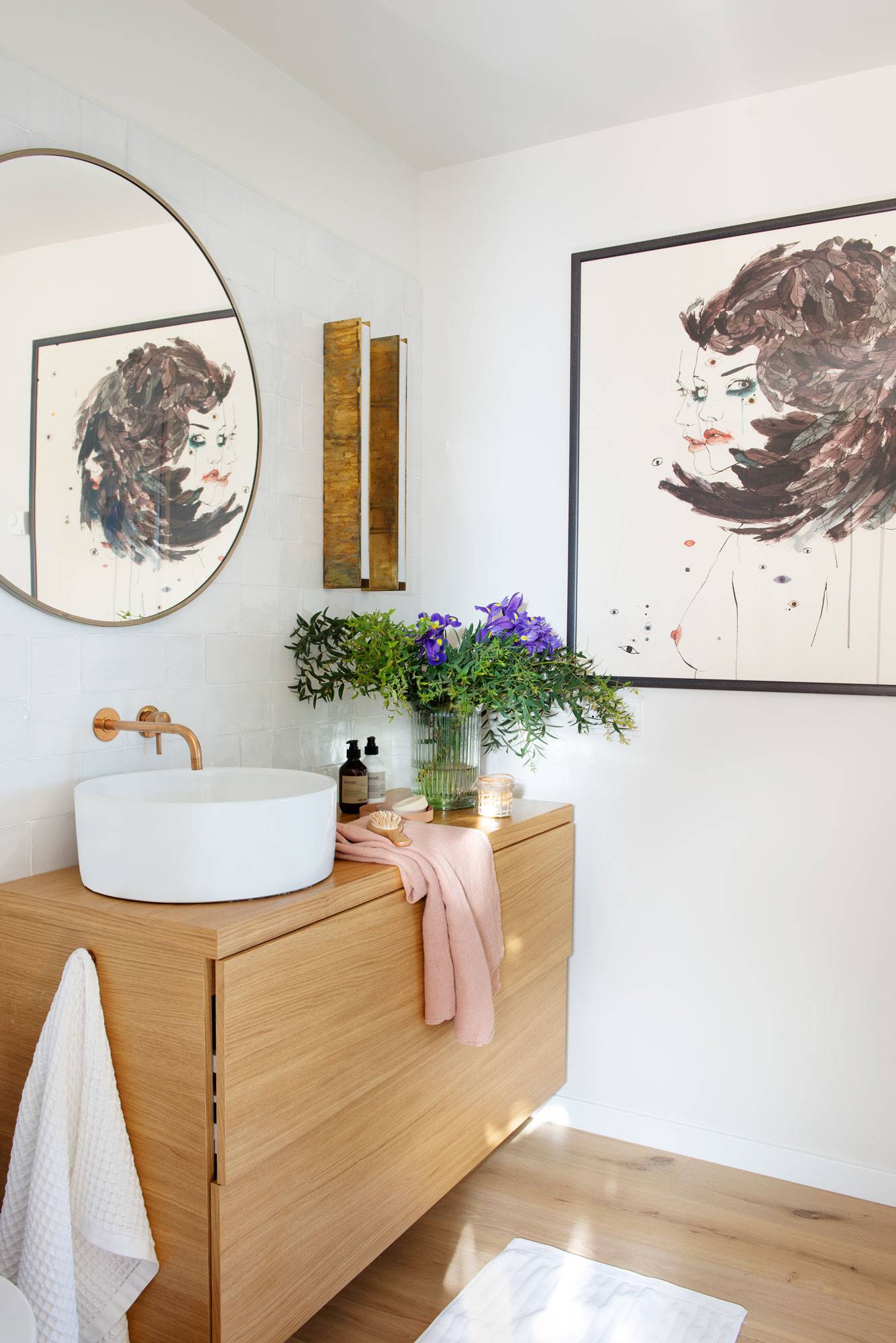 Baño con mueble de madera, espejo redondo y cuadro sobre la pared.