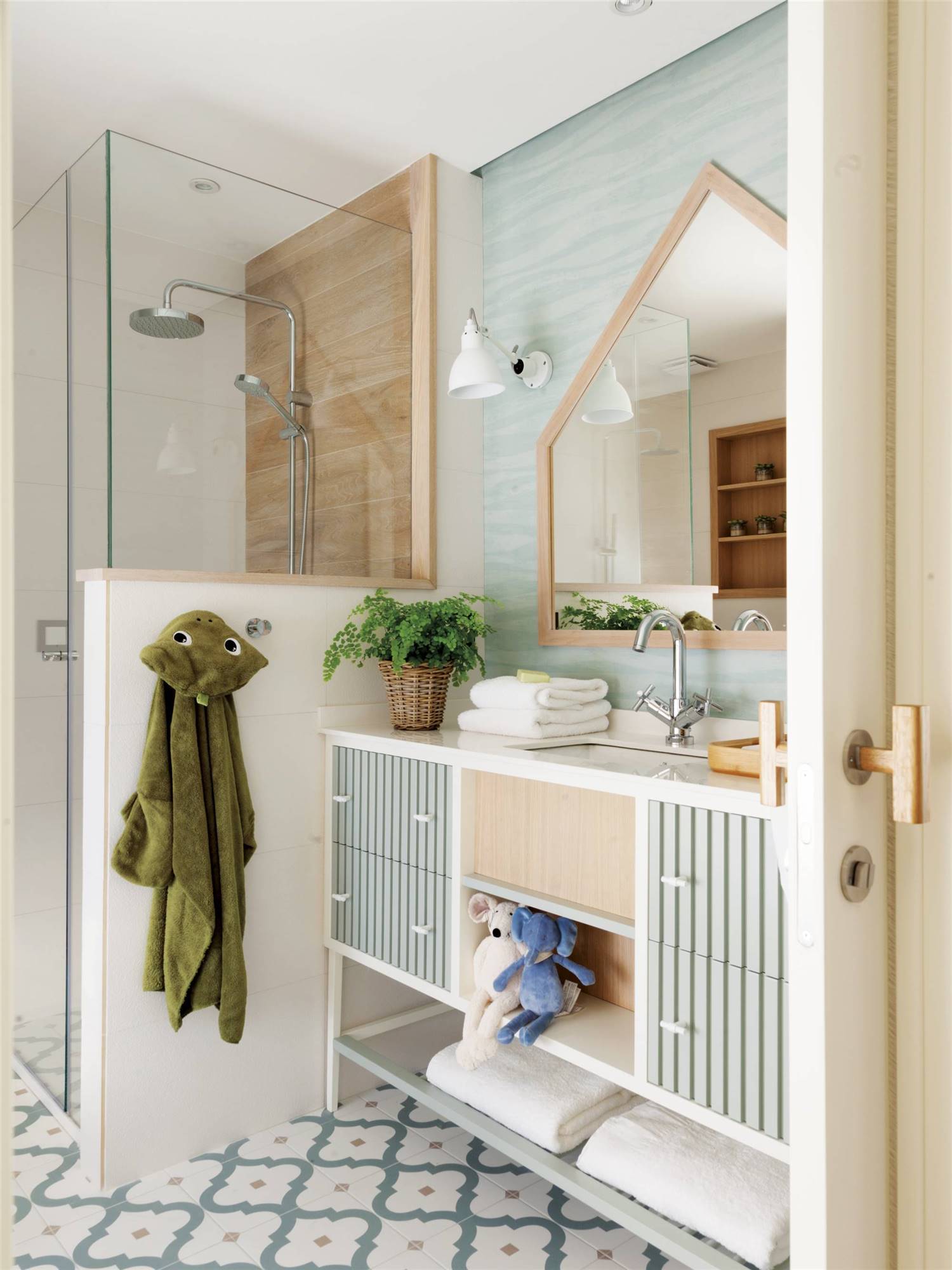 Baño infantil con ducha de obra, baldosa estilo hidráulico, espejo en forma de casita y papel pintado azul aguamarina a juego con el mueble.