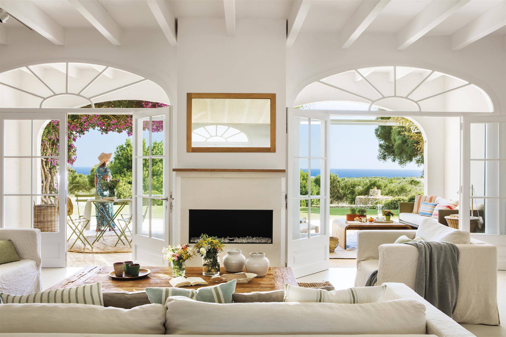 salón de casa de verano con chimenea y grandes ventanales que dan al porche y vistas al mar