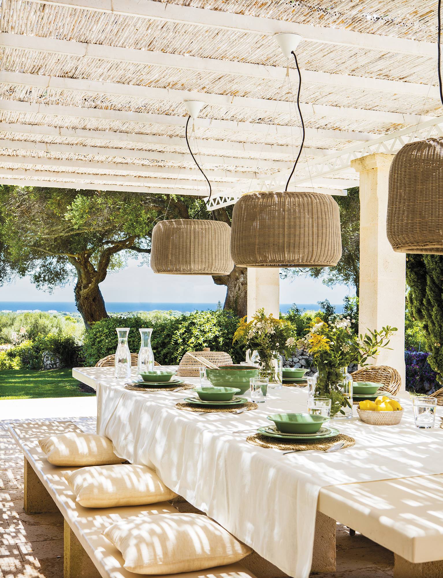 Porche blanco con gran mesa y vistas al jardín y al mar