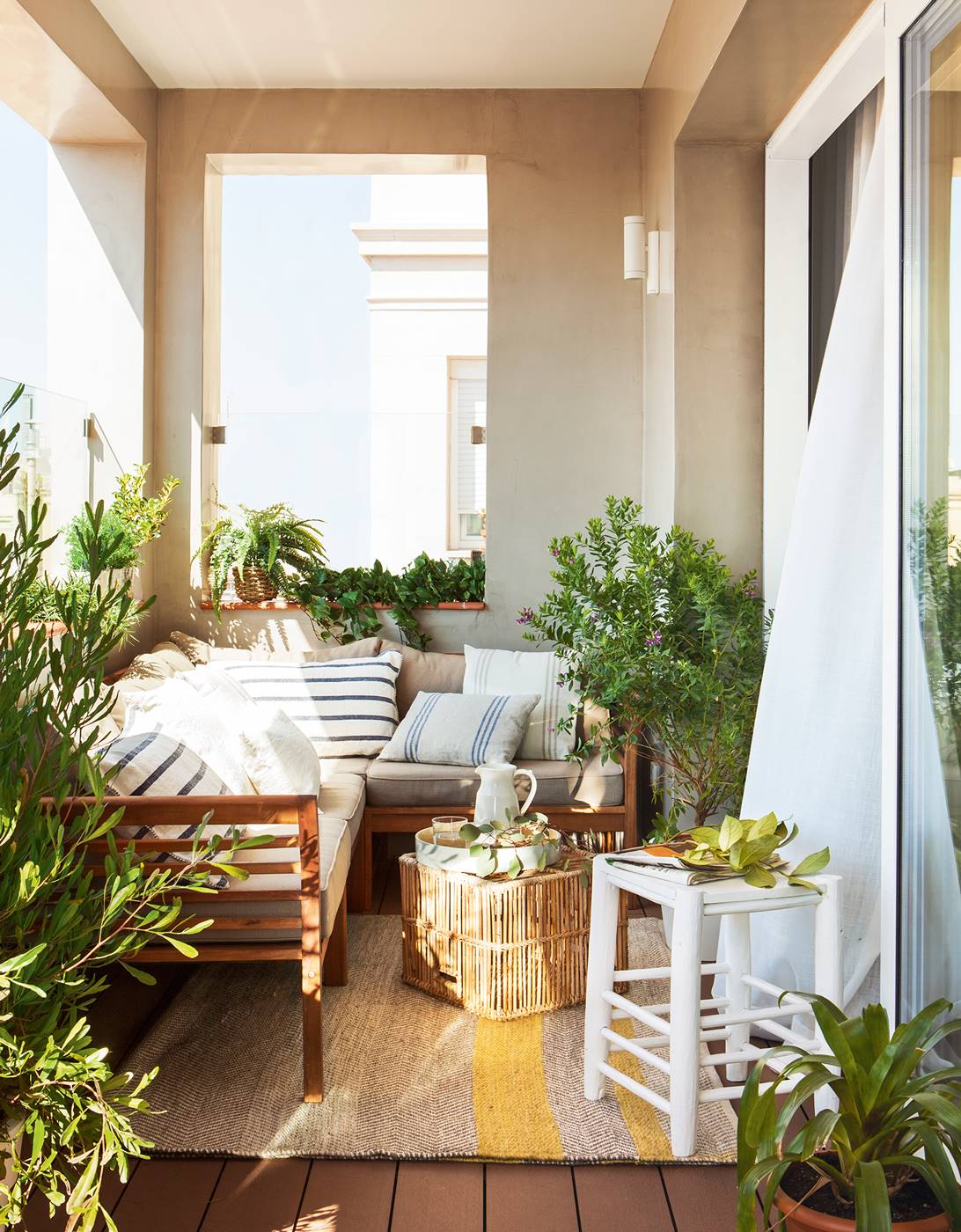Terraza cubierta con sofá rinconero, mesa de centro de caña, taburete de madera y cojines vintage a rayas, y plantas 420681