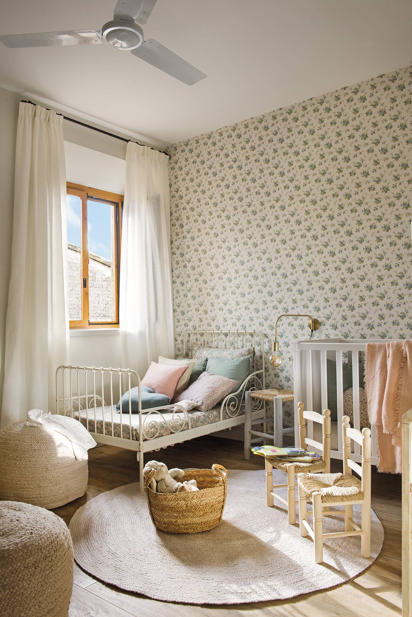 Habitación infantil de estilo campestre con papel pintado floral en tonos verde, cama de forja blanca y decoración de fibras naturales