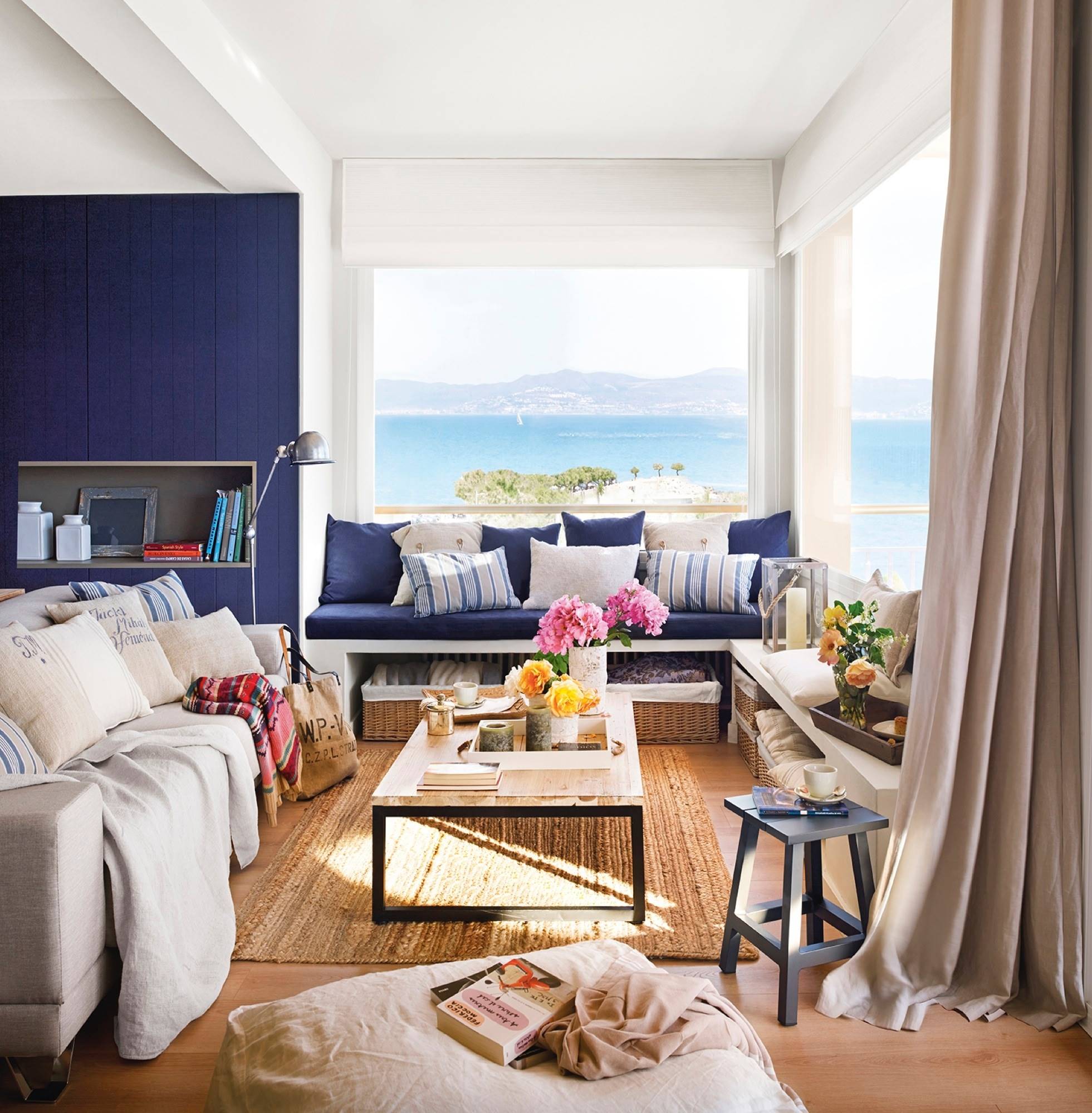 Salón con vistas al mar en blanco y azul con sofá, banco bajoventana y mesa de centro industrial 407813
