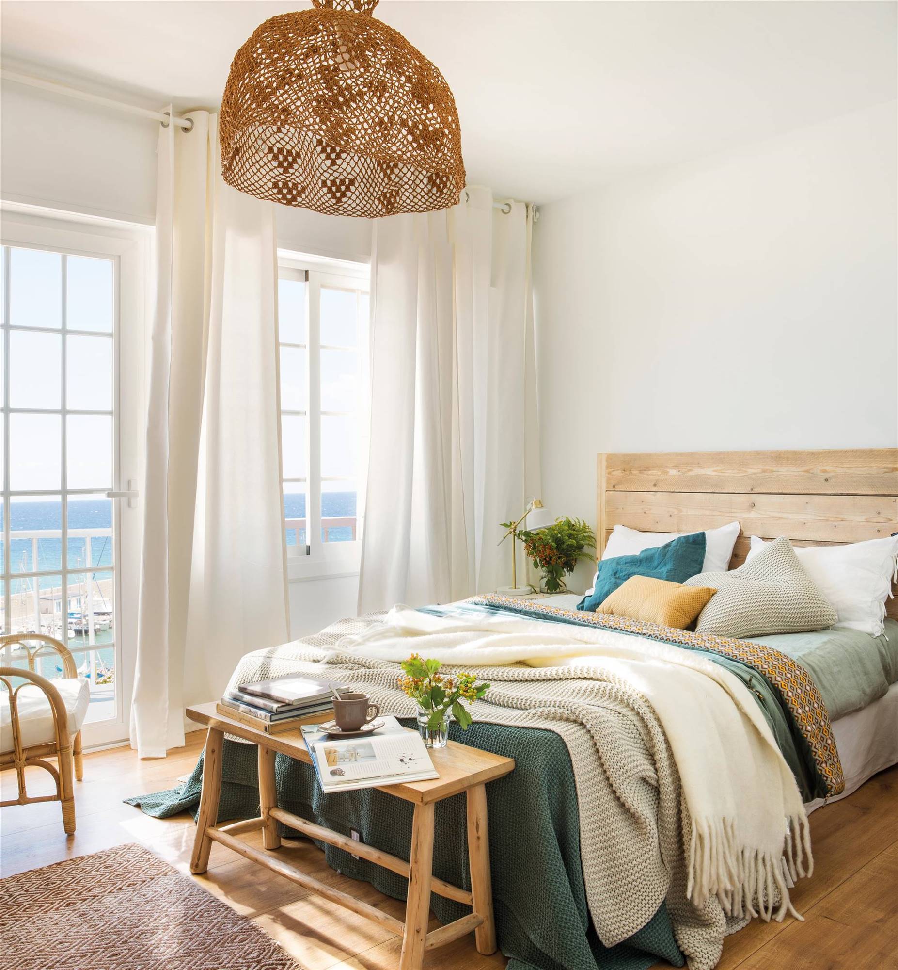 Dormitorio con cabecero y banco a pie de cama de madera y gran lámpara de fibras naturales.  