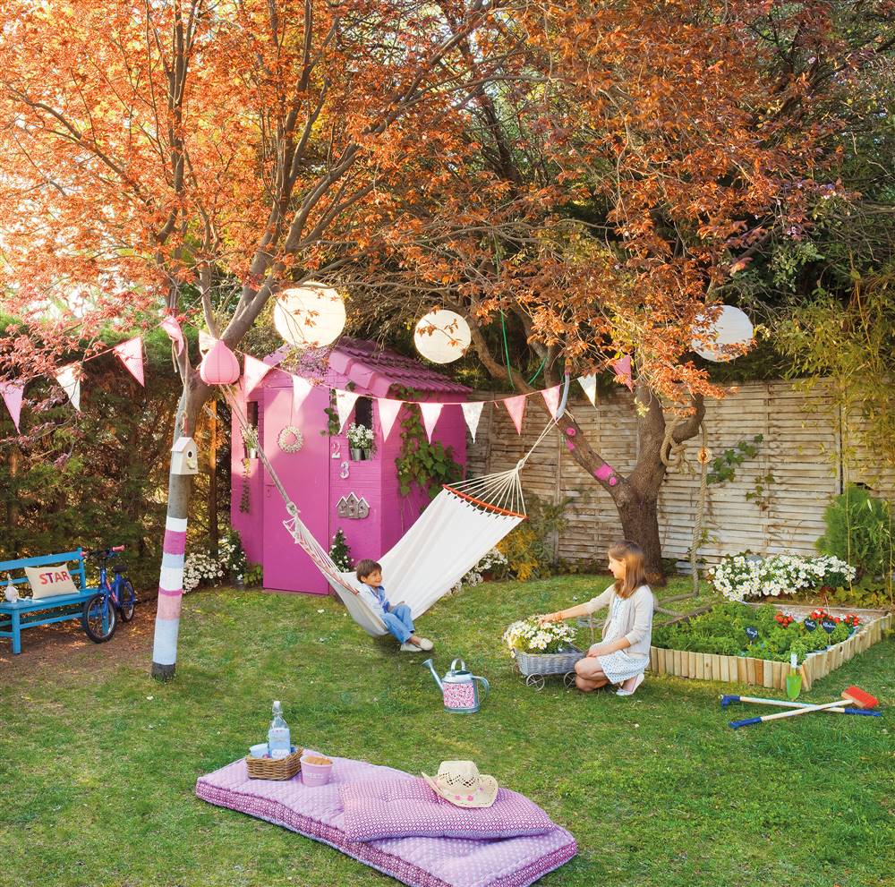 JArdín con casita de madera rosa, guirnaldas entre los árboles, huerto, hamaca con niño y mujer sentada en el césped_00343813b