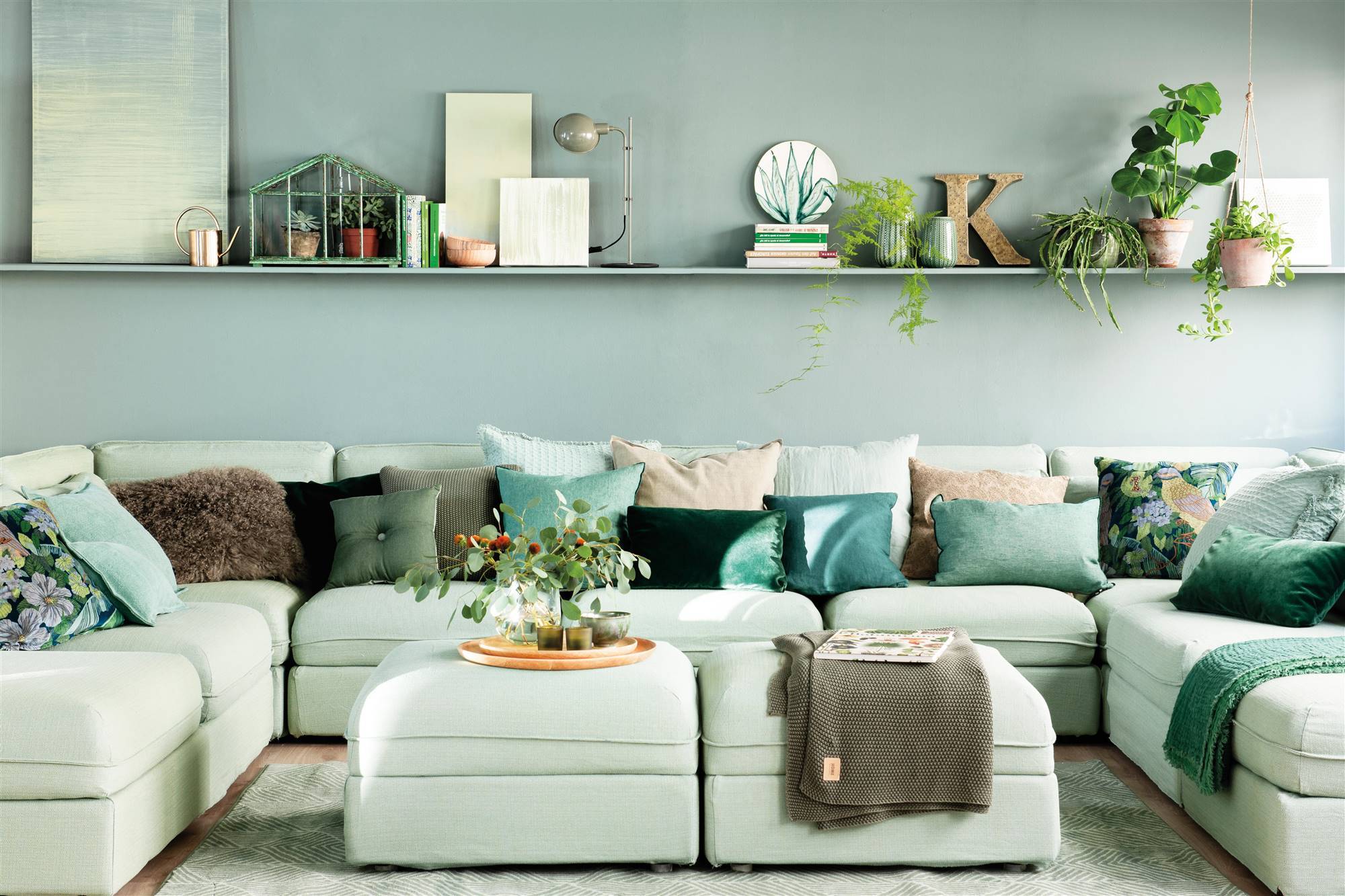 Salón con sofá en U de color verde y cojines de varios tonos de verde y blanco. 