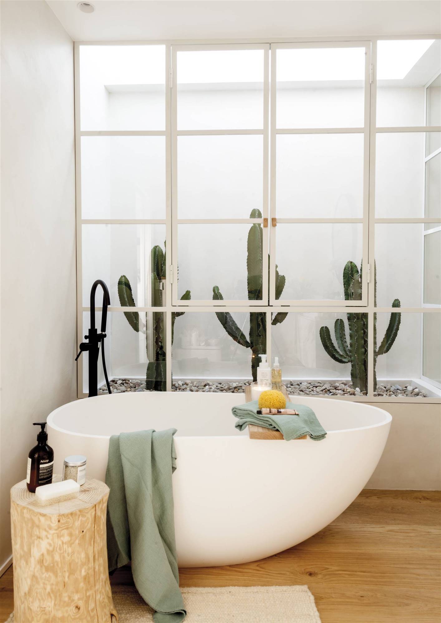 Baño con bañera, toallas verdes y plantas. 