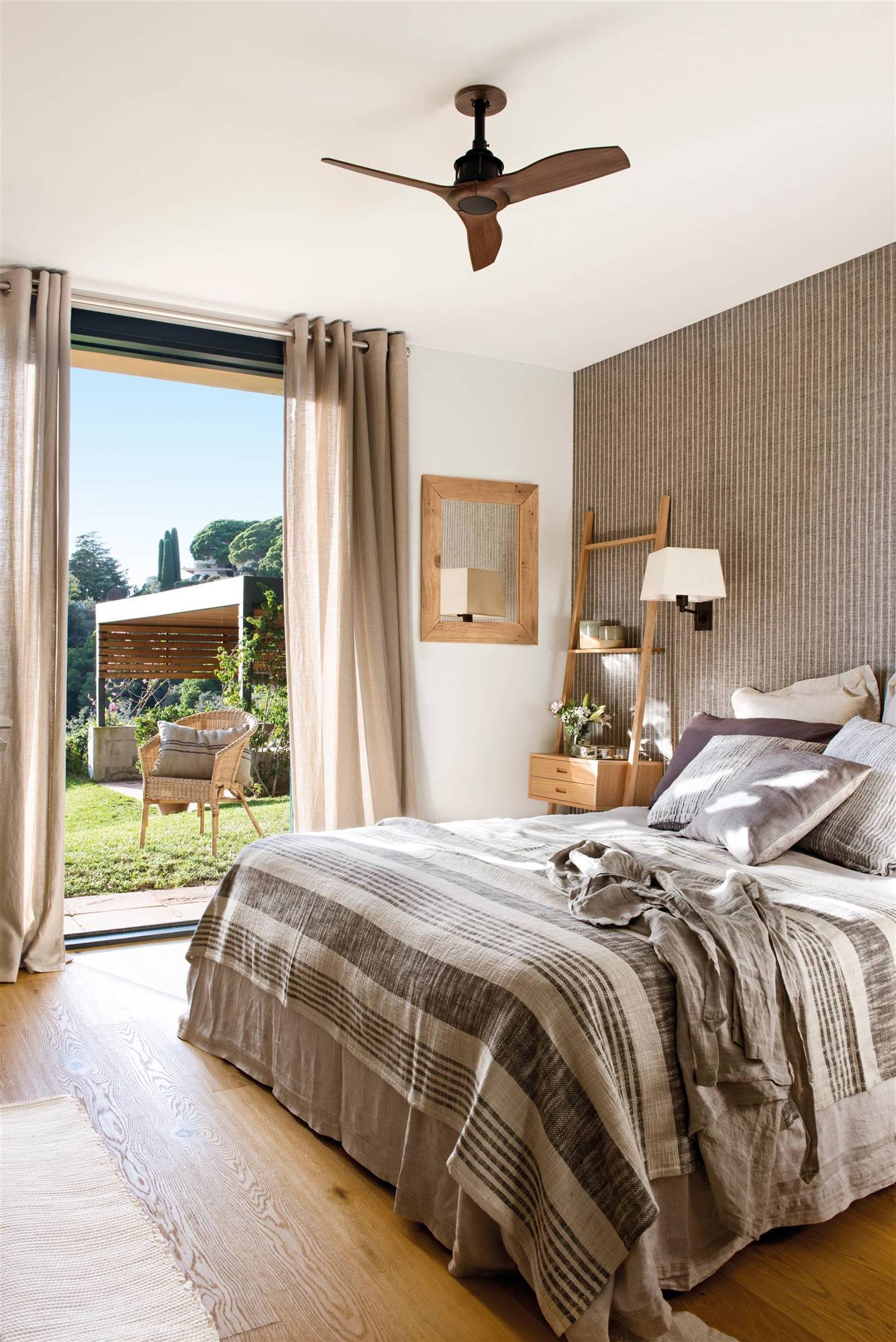 Dormitorio de verano con ventilador de techo y ropa de cama étnica en blanco y gris. 