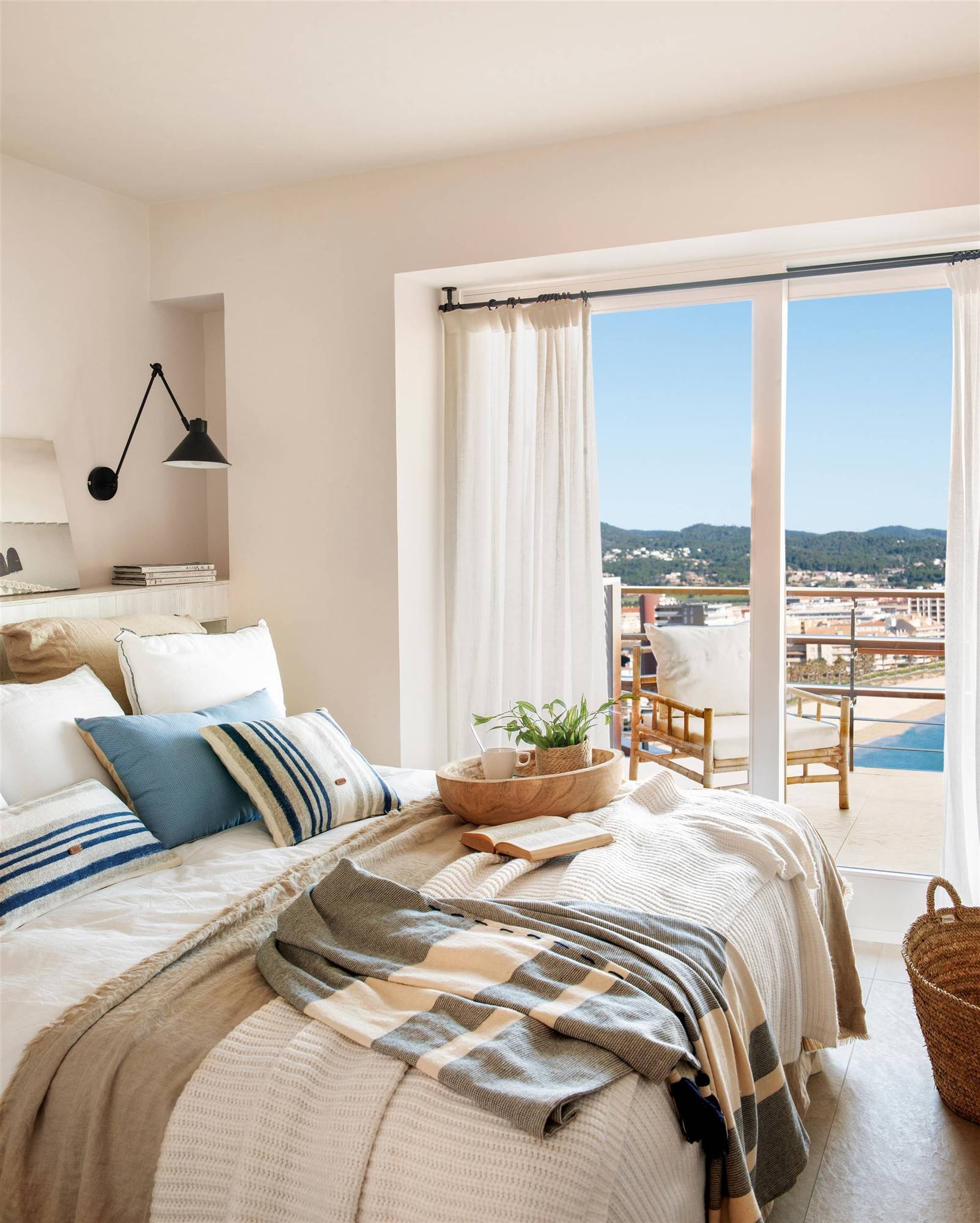 Dormitorio de verano con vistas a la playa y cojines a rayas azules y blancas. 