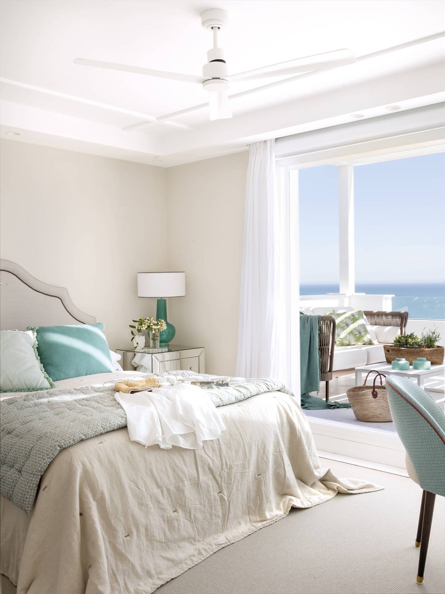 Dormitorio de verano con ropa de cama en blanco y aguamarina con ventilador de techo. 