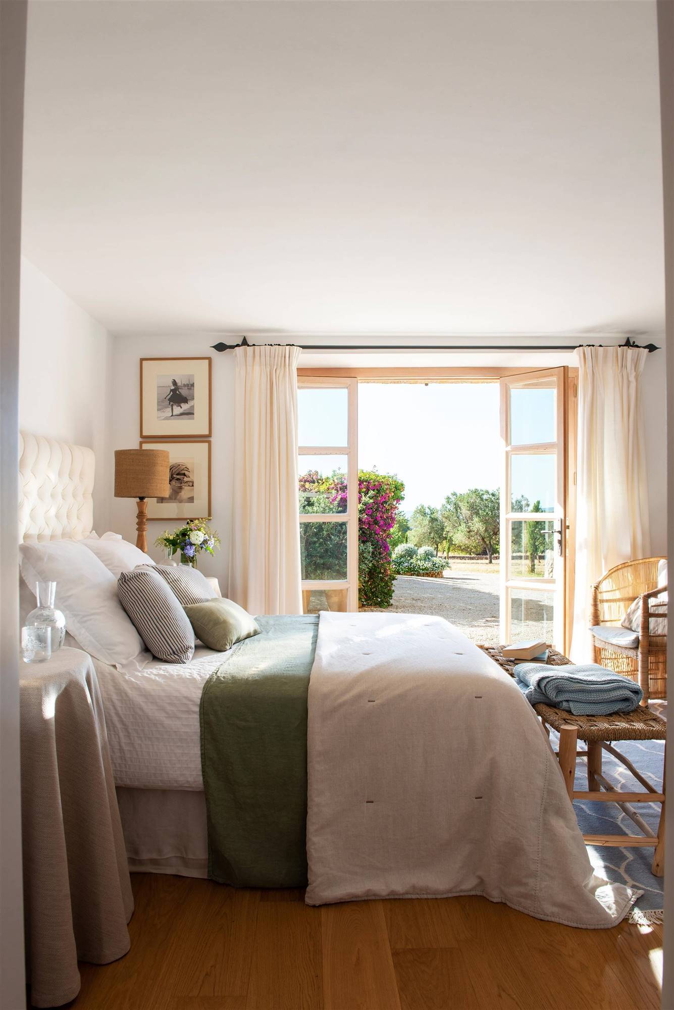 Dormitorio de verano con acceso al jardín, cabecero de capitoné blanco y ropa de cama verde y blanca. 