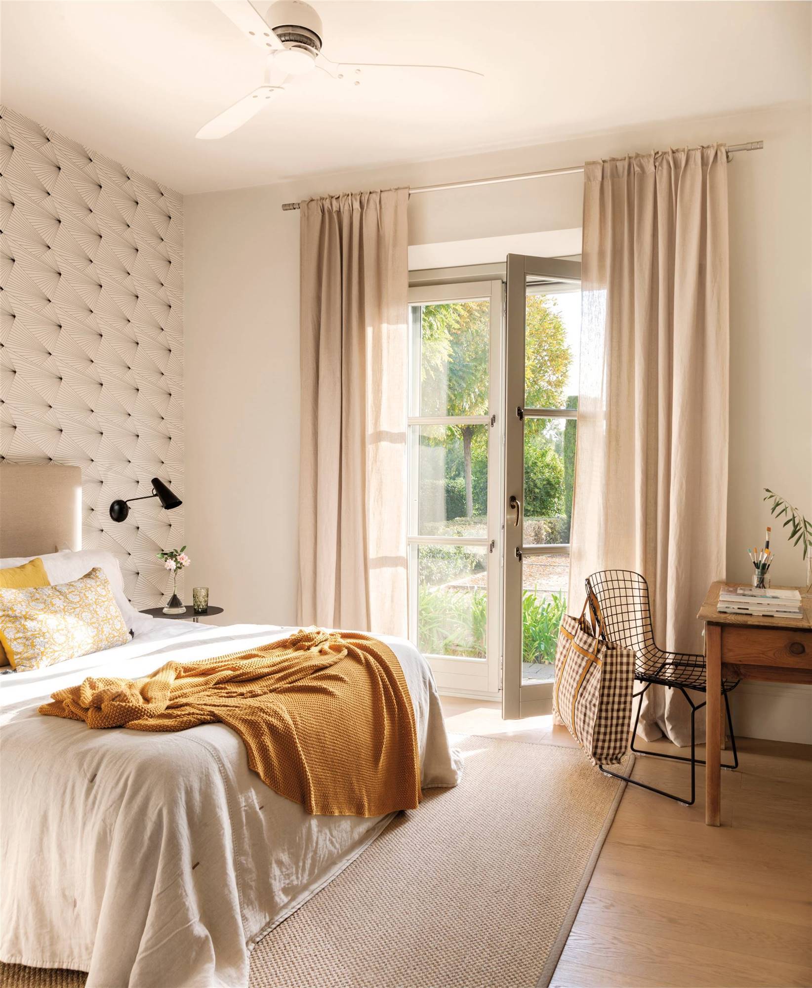 Dormitorio de verano con papel pintado geométrico en la pared de cabecero y ropa de cama blanca y mostaza. 