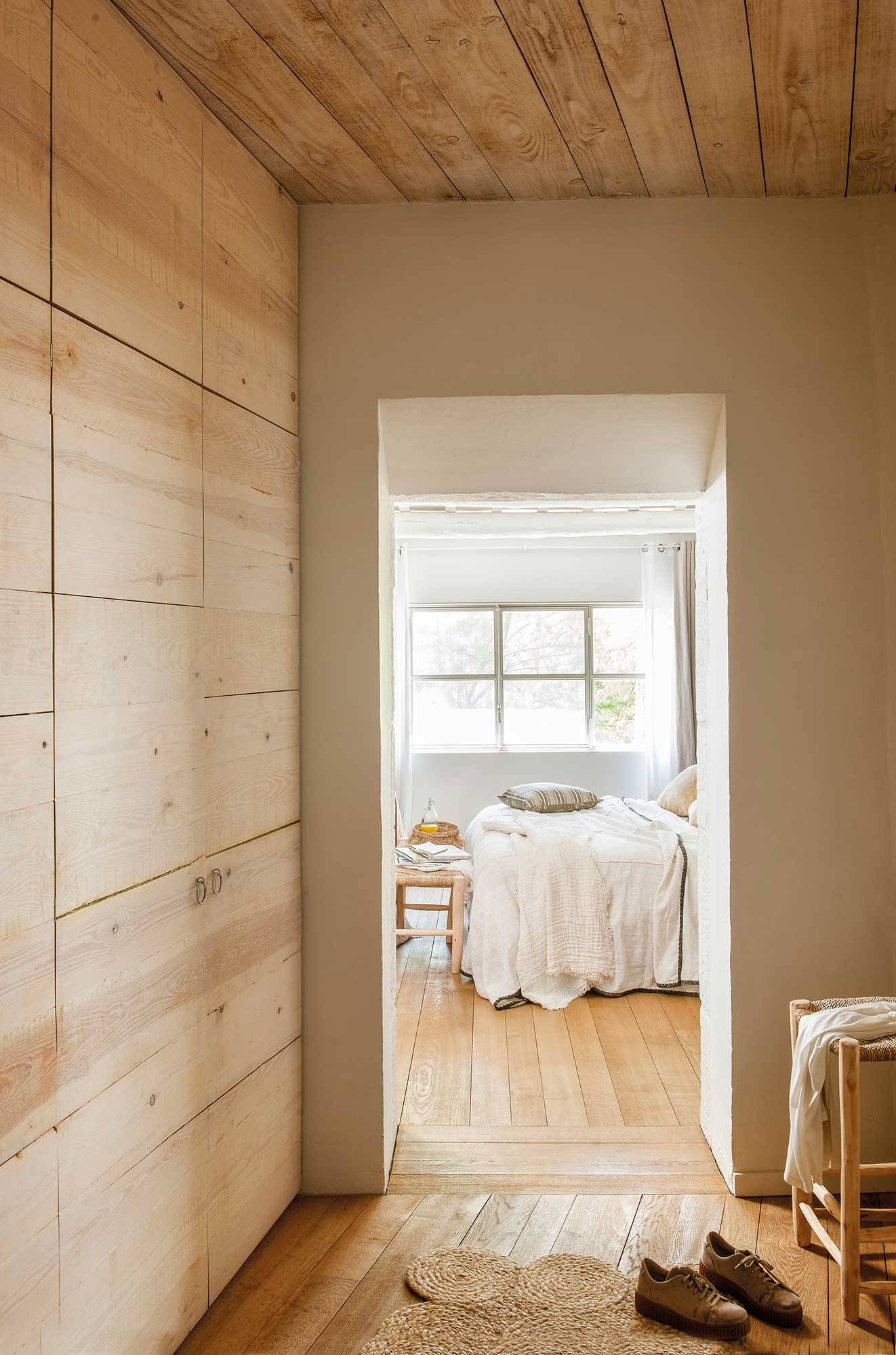Vestidor con armario de madera y dormitorio al fondo. 