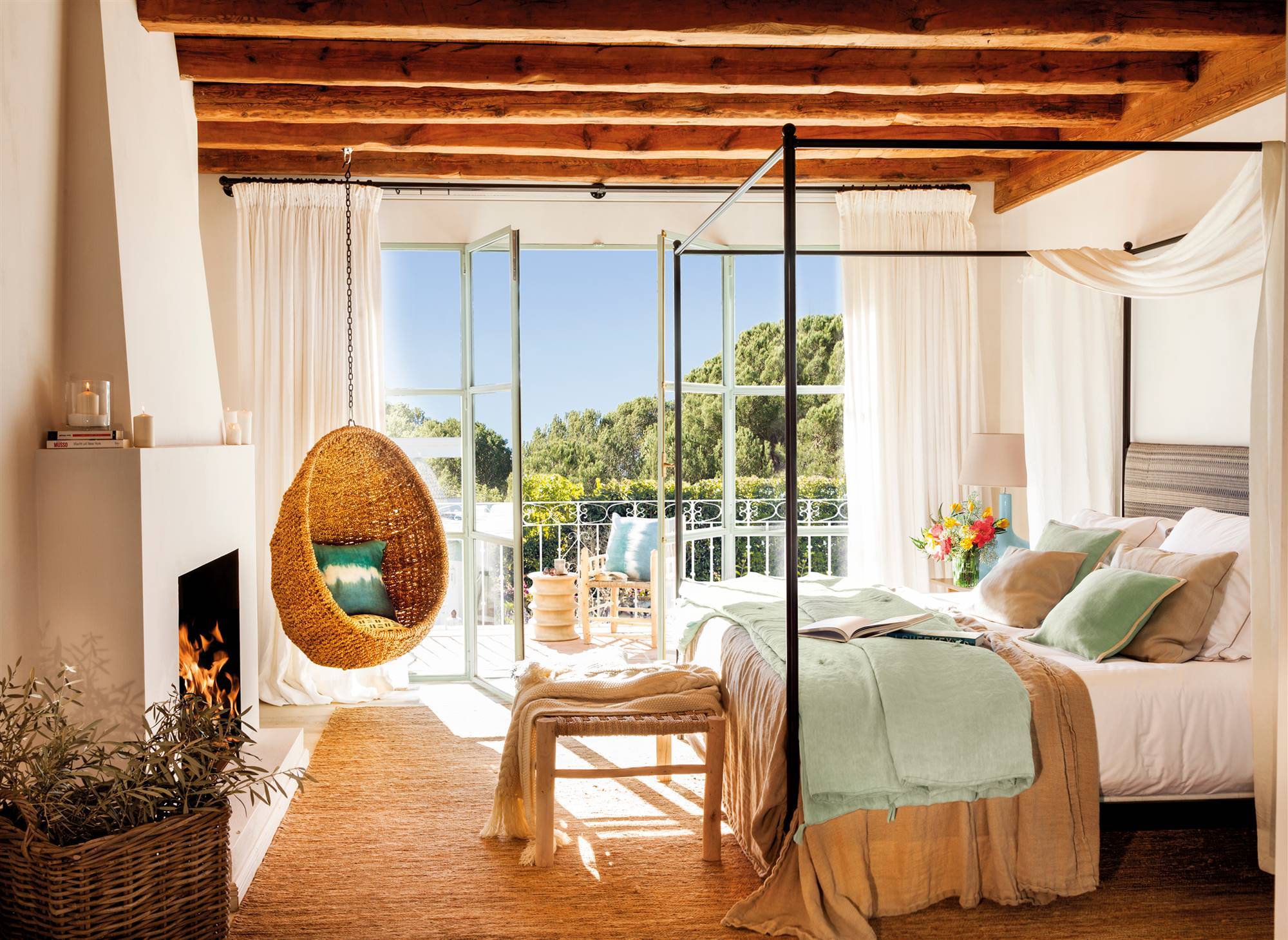 Dormitorio con cama con dosel metálico, columpio de fibras, alfombra de fibras, vigas de madera, chimenea y acceso a la terraza. 