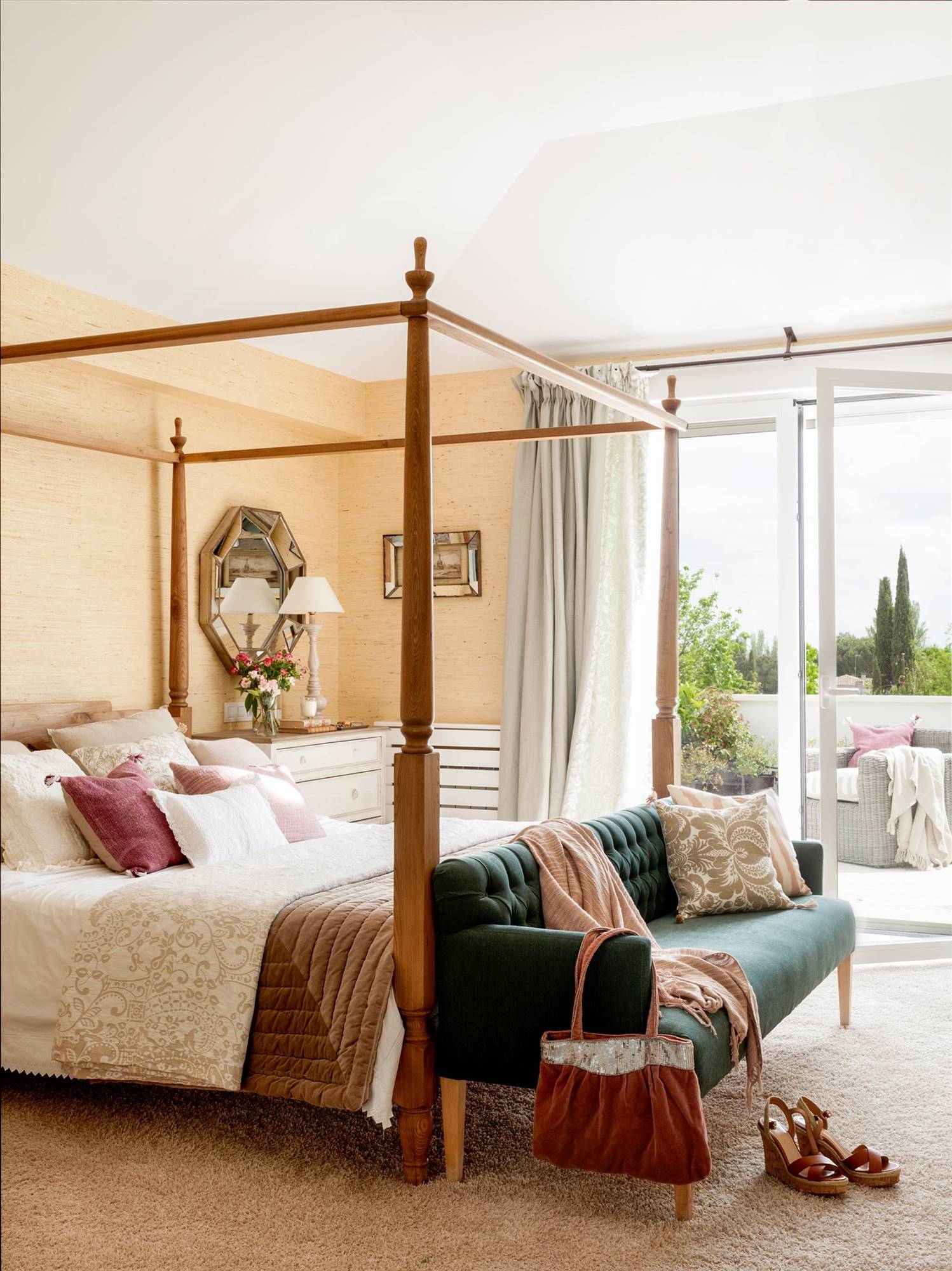 Dormitorio de estilo clásico con dosel de madera y sofá con tapizado capitoné verde a los pies. 