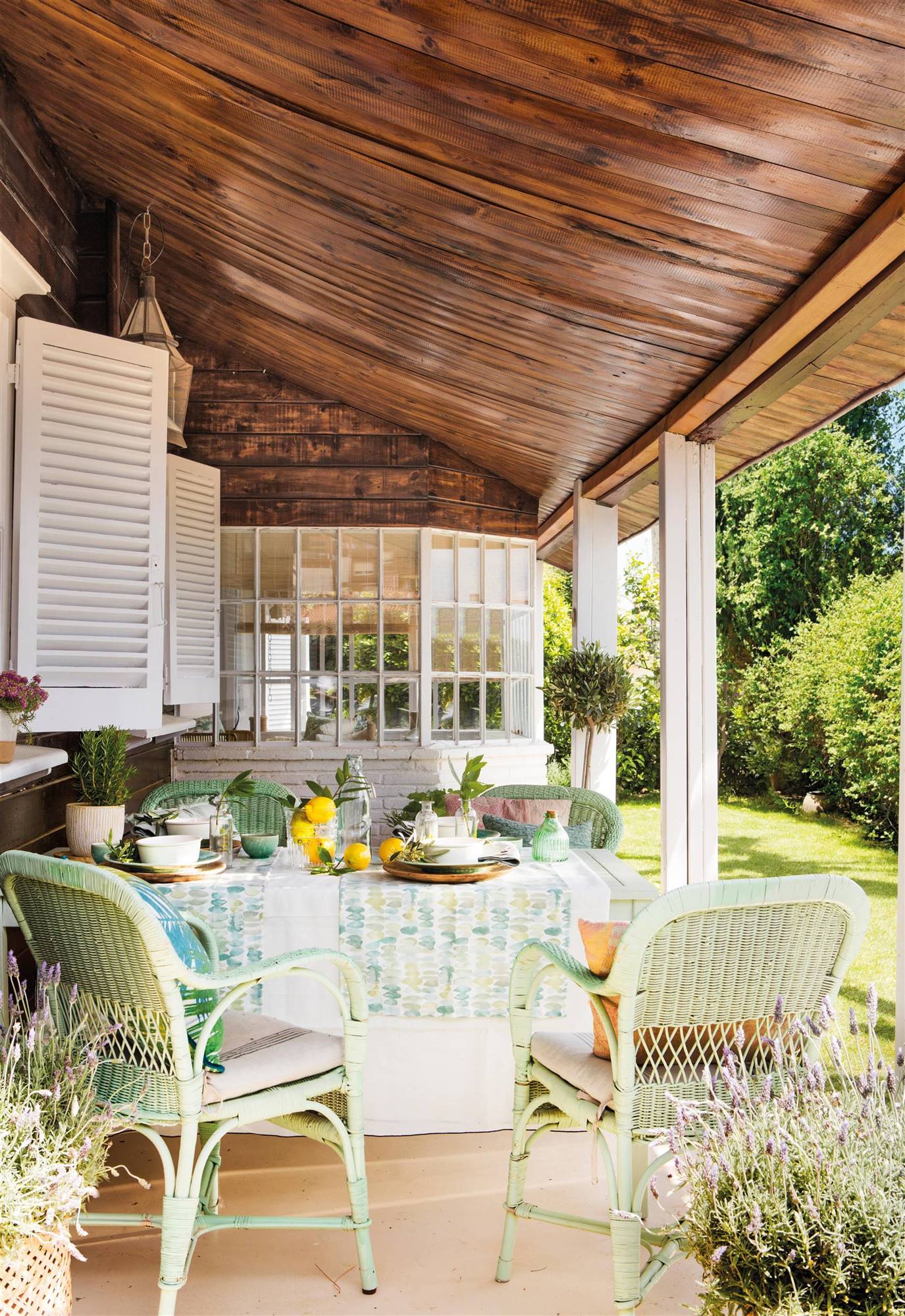 Un porche de color verde agua con sillas y mantel a juego con el jardín. 