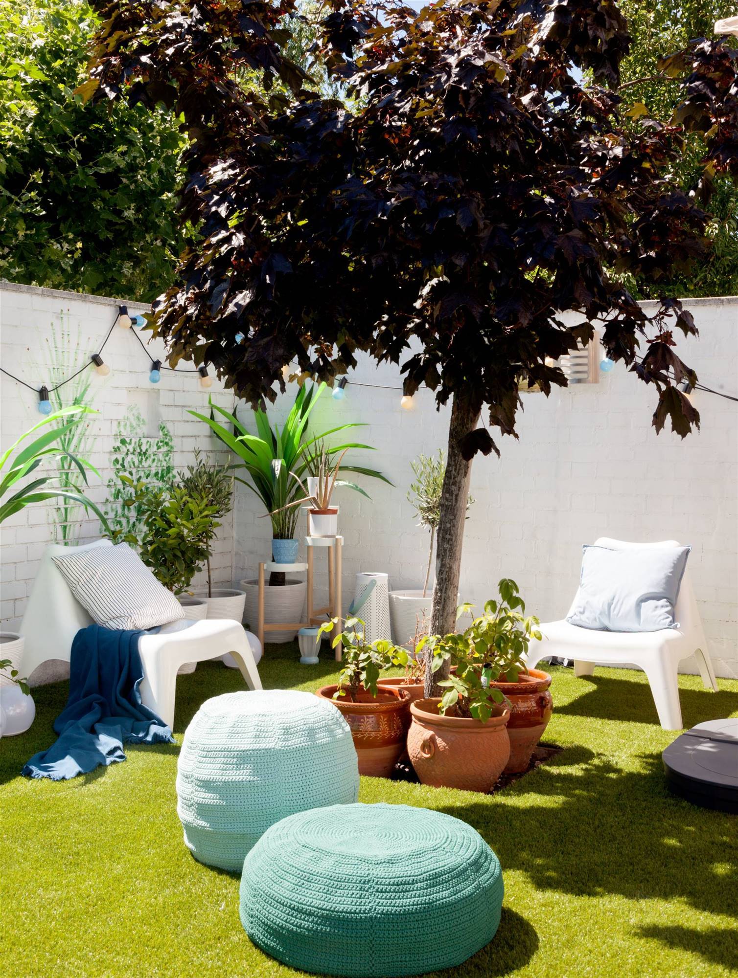 Terraza con chill out con butacas blancas, puffs azules y macetas con plantas.