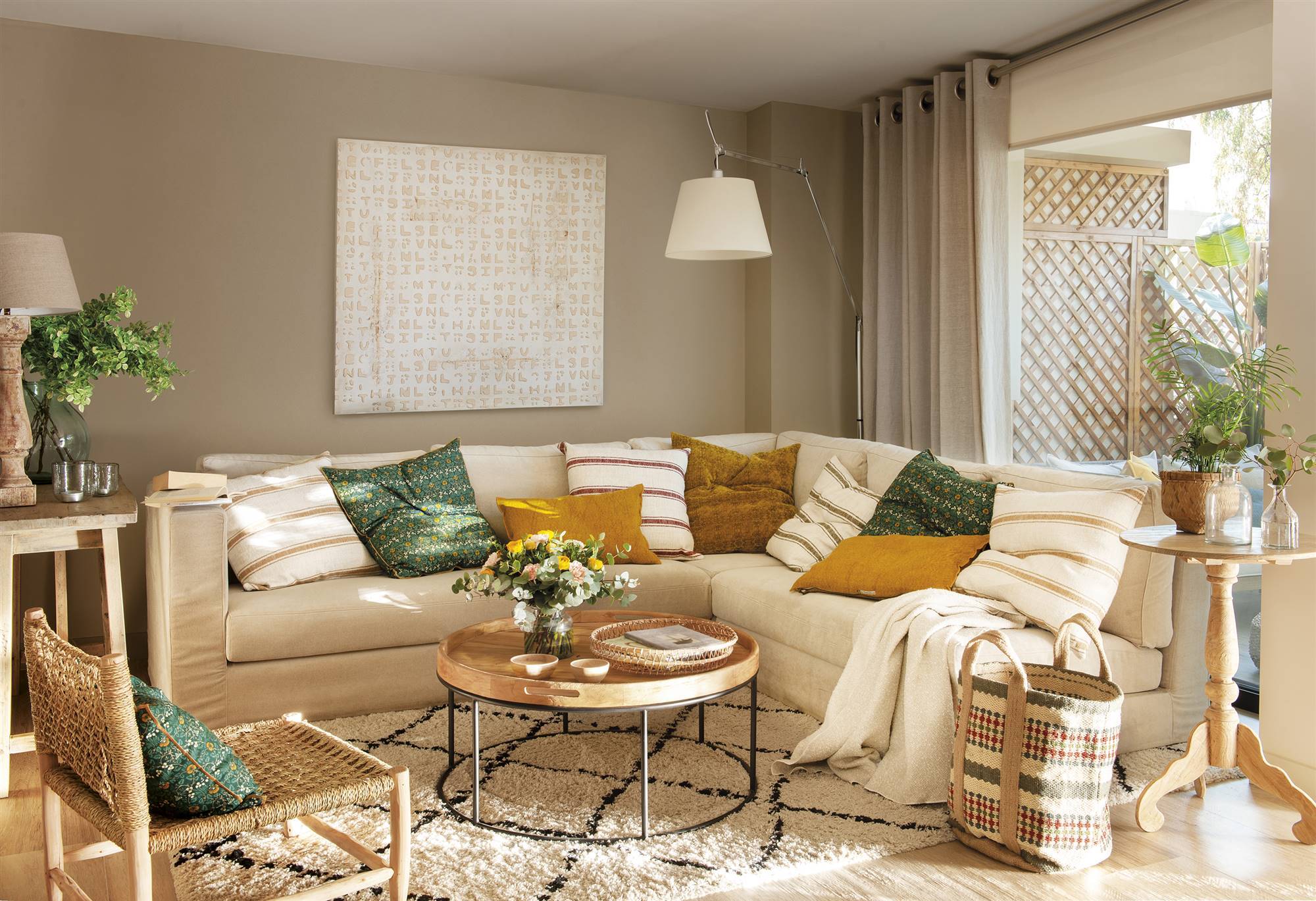Salón con sofá en L beige, alfombra kilim, mesa de centro redonda con sobre de madera y patas de hierro y una butaca de fibras