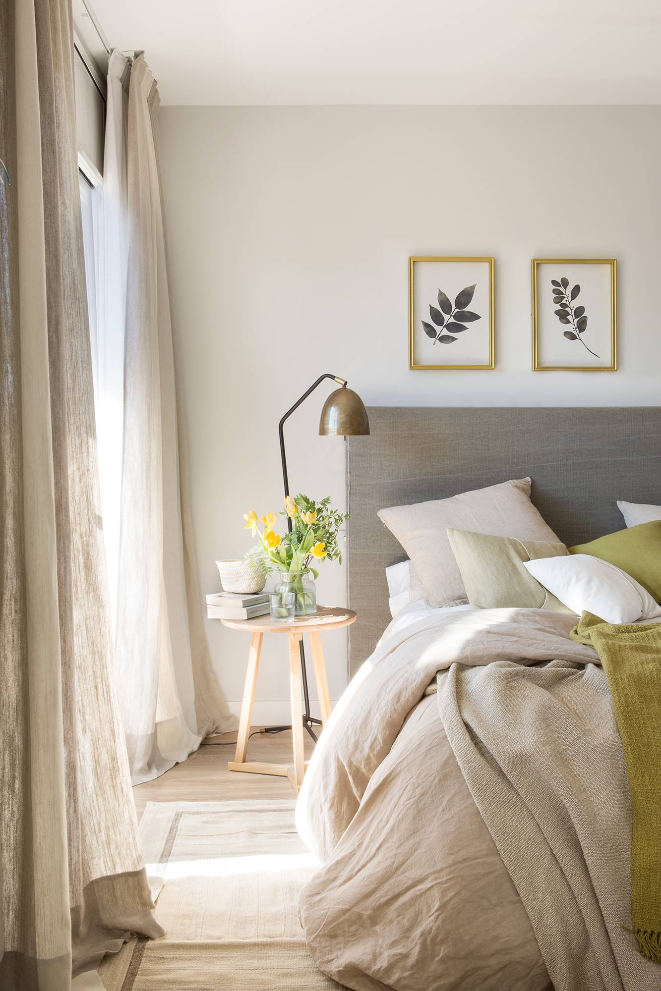 Dormitorio decorado en gris y verde con cabecero de tela, mesita de noche tipo taburete de madera, lámpara de mesa de latón envejecido y cuadros botánicos sobre el cabecero 00469272 Ob