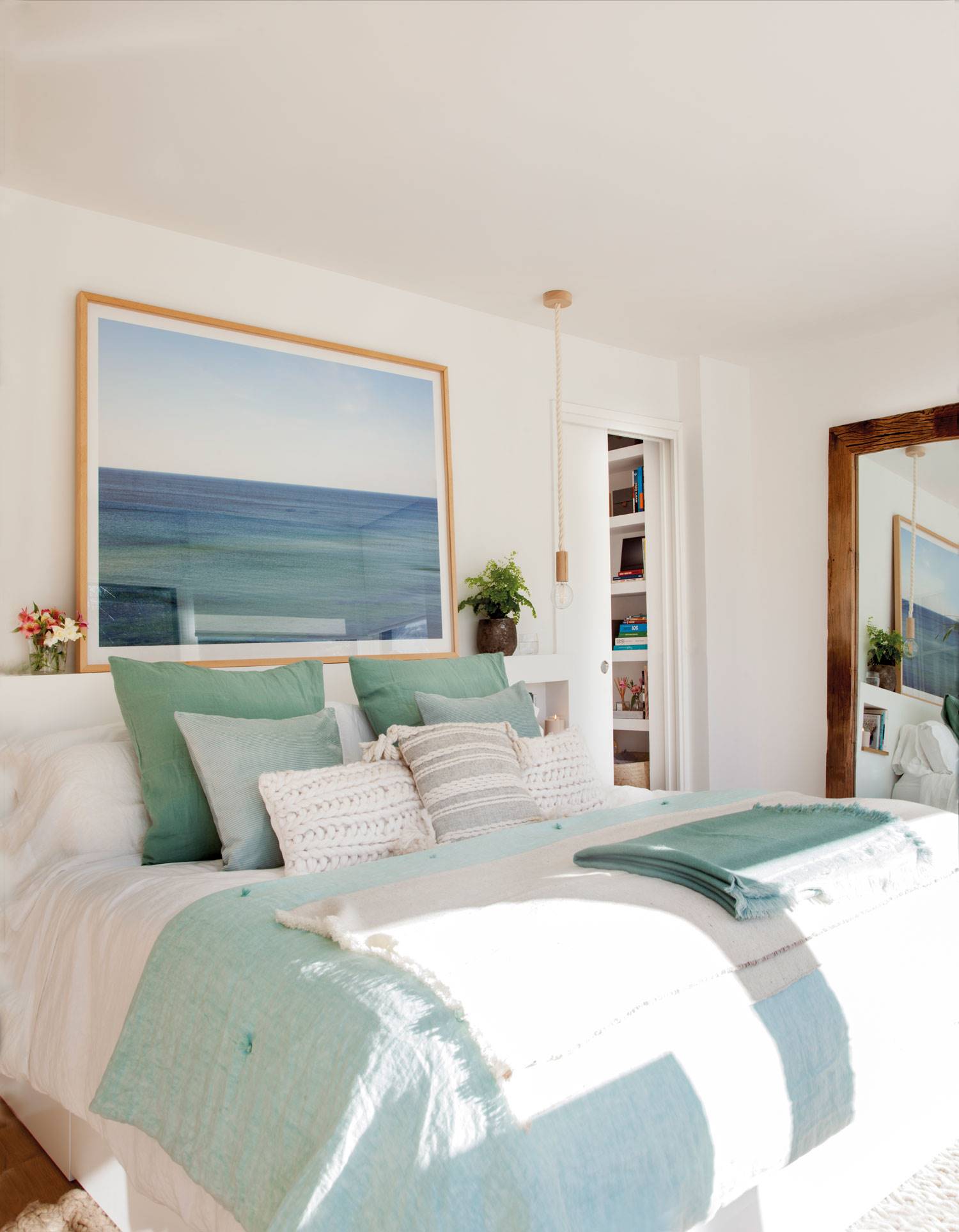Dormitorio con cabecero de obra blanco y hornacinas, un cuadro grande de un paisaje marino y lámparas suspendidas 503768