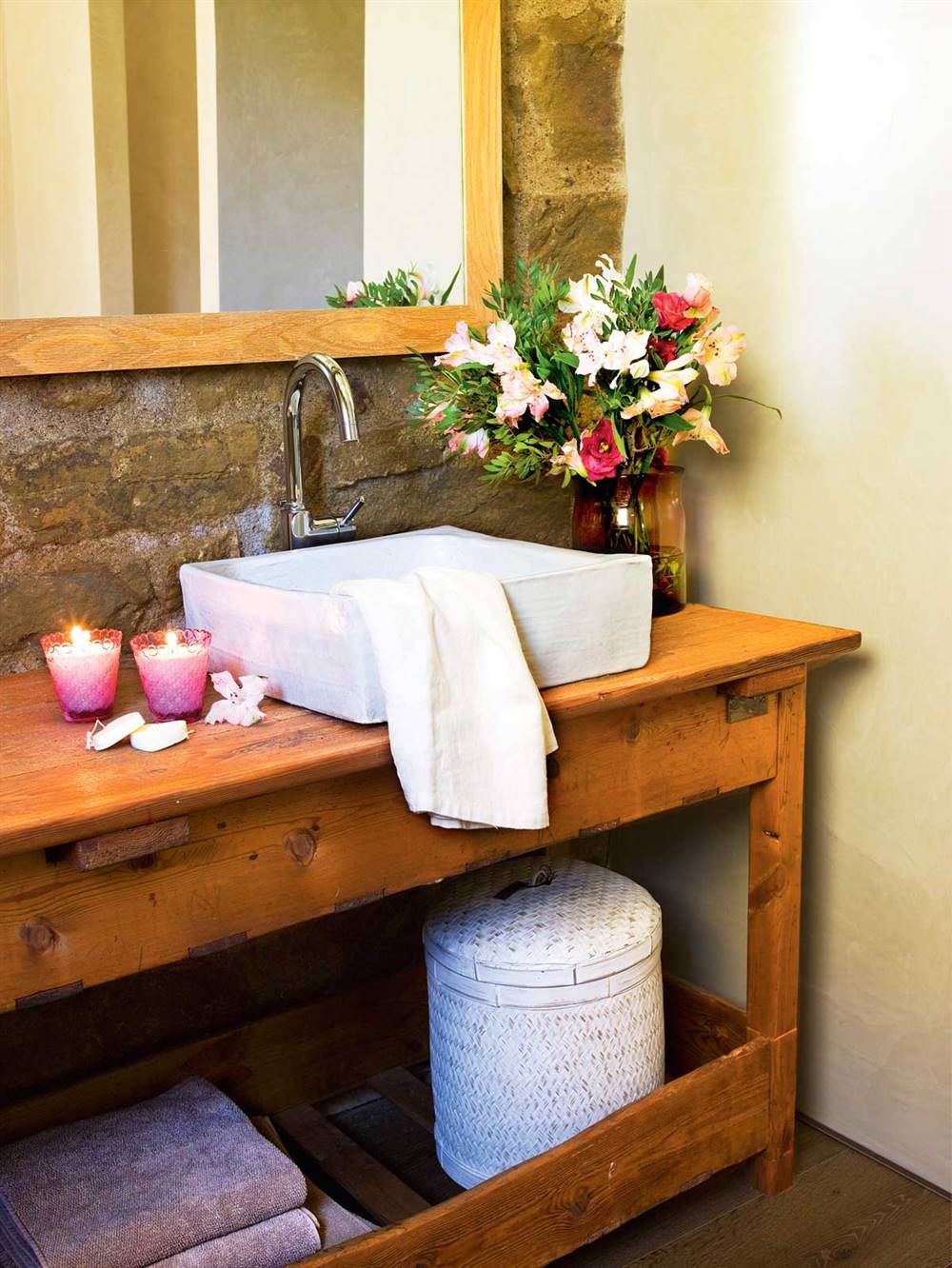 Baño rústico con mueble bajolavabo de madera, velas, espejo, pared de piedra y flores- 391516