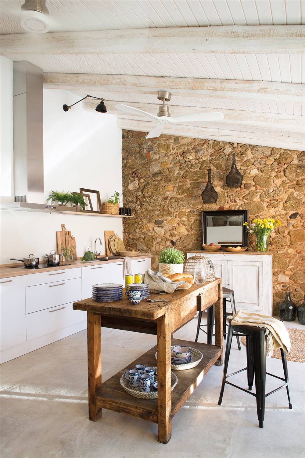 Cocina blanca con pared de piedra, vigas de madera en blanco e isla central con mueble recuperado_ 00438574