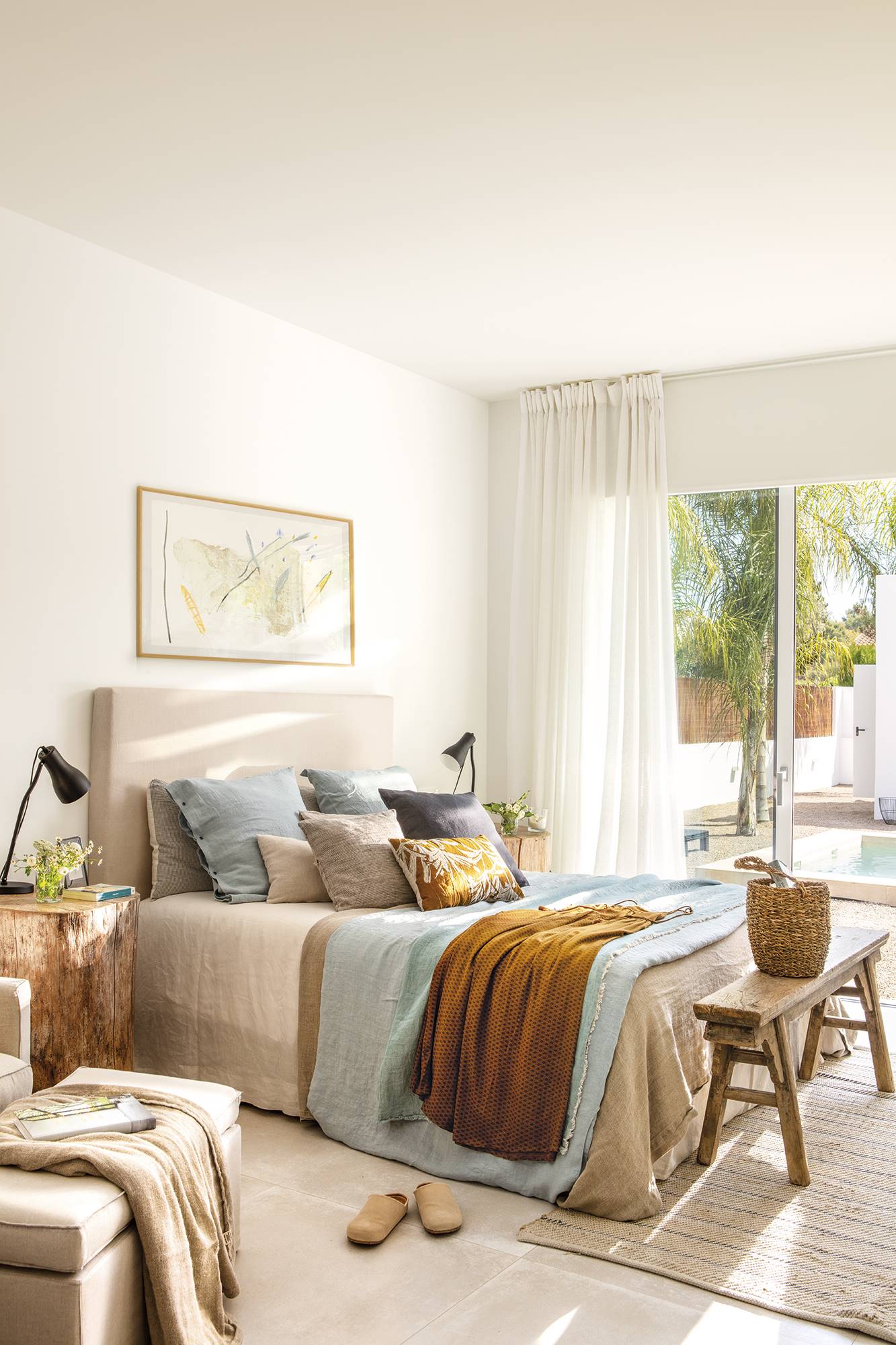 Dormitorio con cabecero tapizado beige y banco de madera a pie de cama.