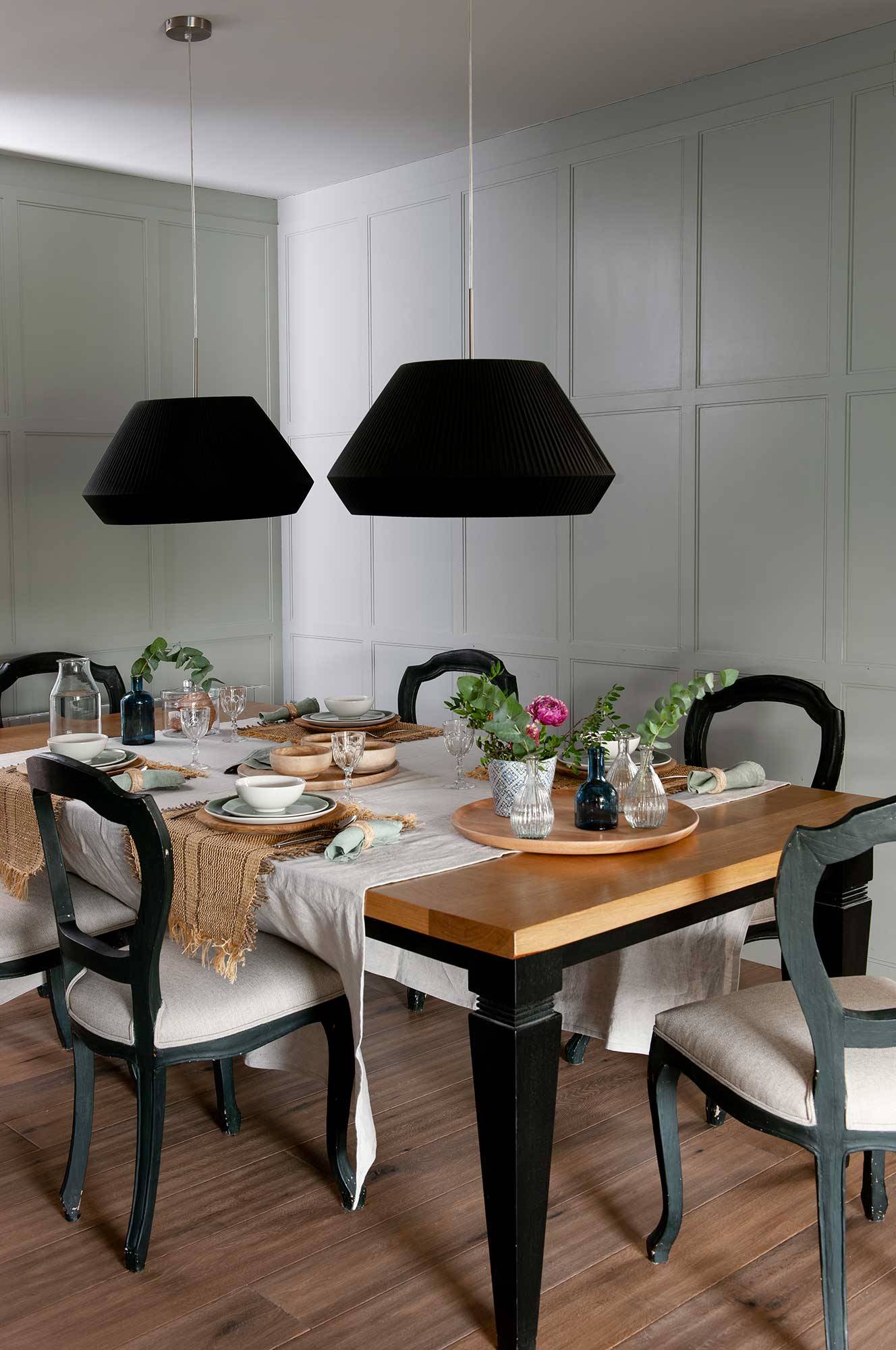 Comedor con mesa de madera y patas negras, sillas y lámparas de techo negras.