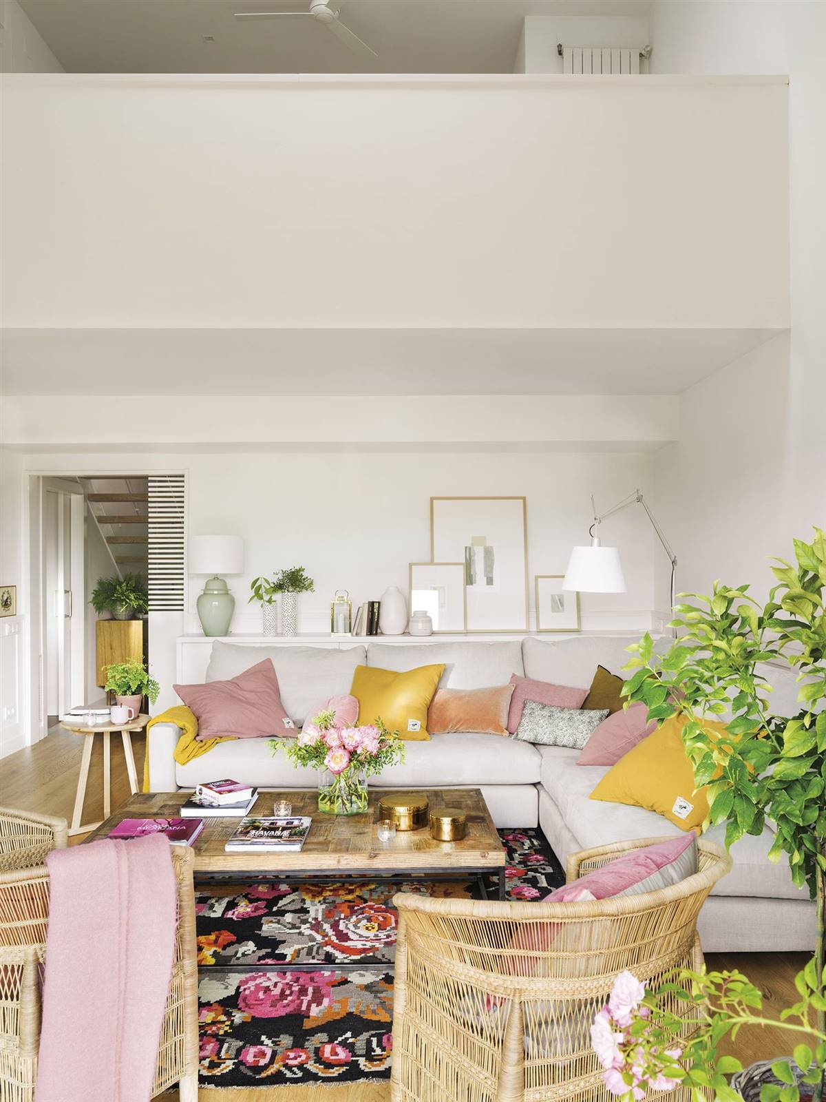 Salón pequeño con paredes blancas, sofá gris en ''L'', mesa auxiliar de madera, alfombra con motivos florales y textiles en rosa y mostaza