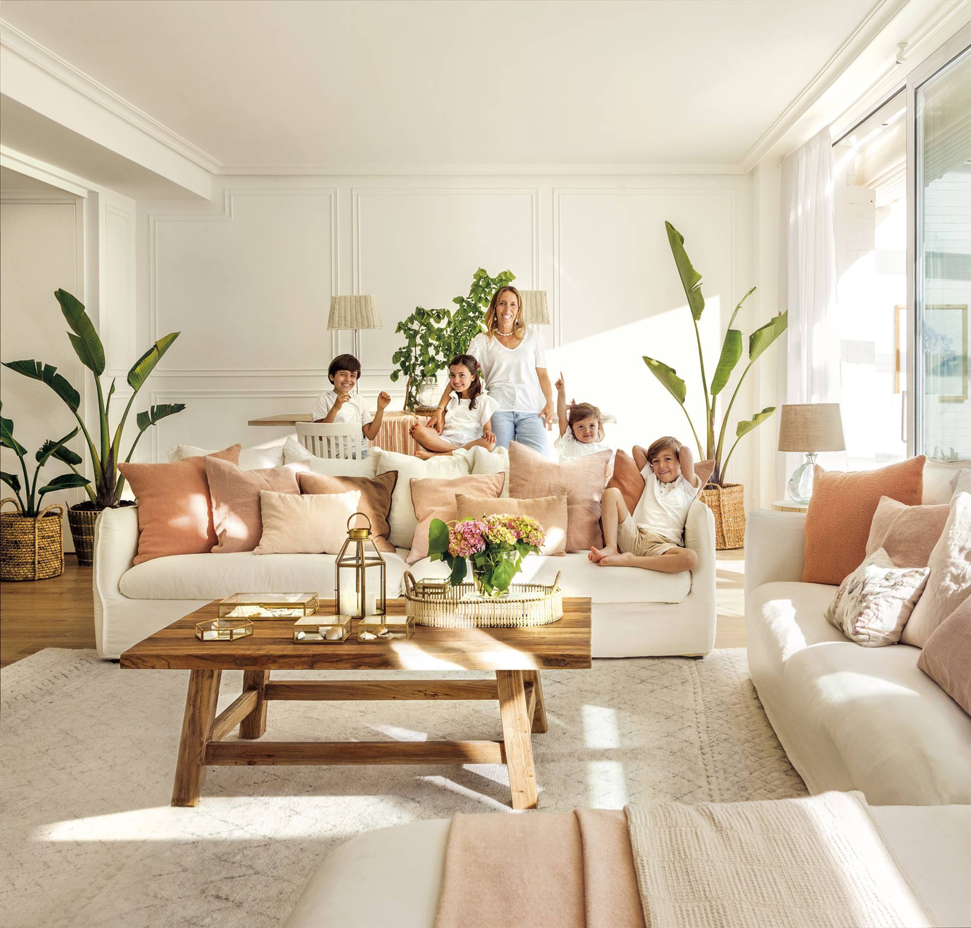 Salón con sofás blancos con cojines, mesa de centro de madera y plantas de interior.