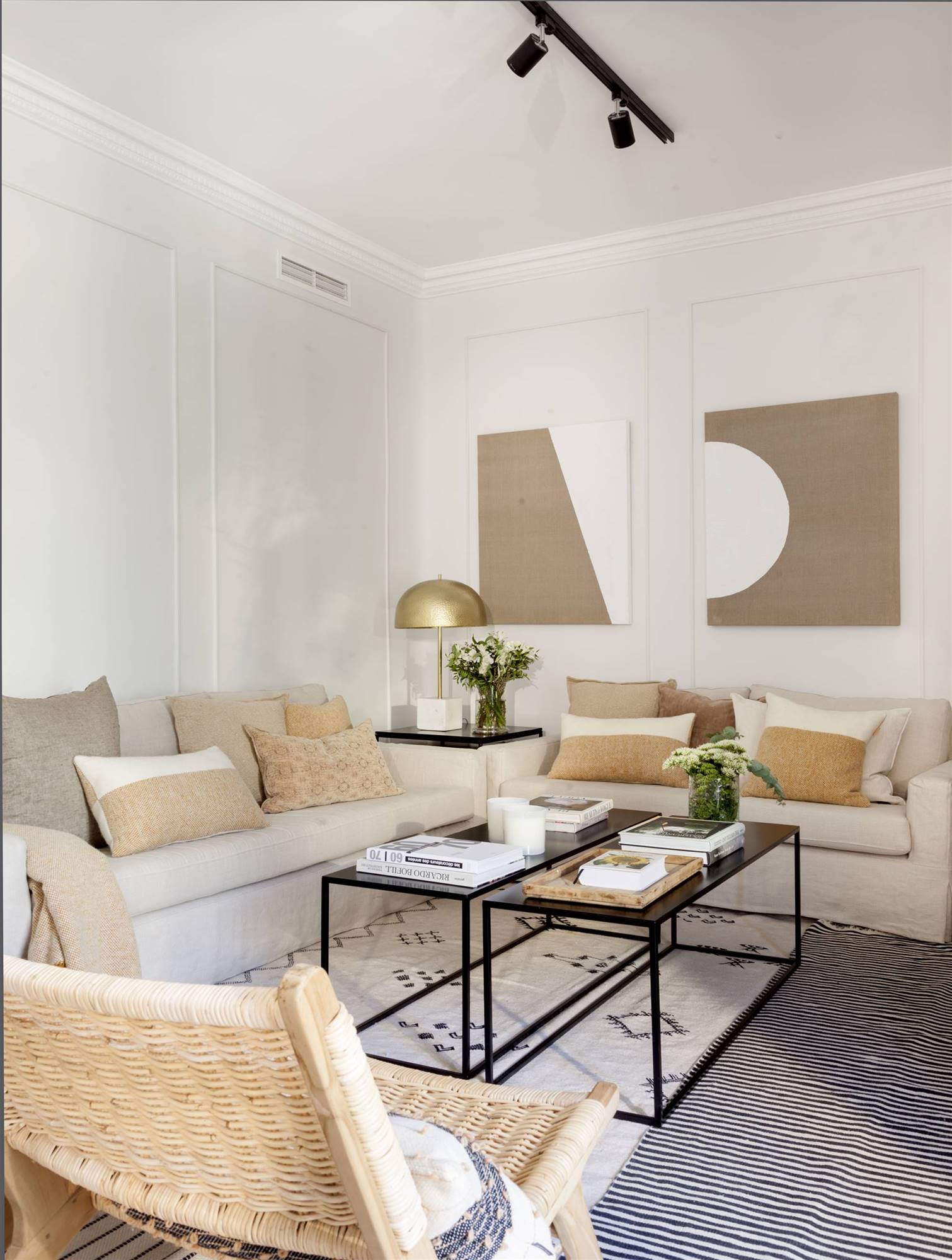 Salón con paredes blancas, sofás beige y mesas de centro de color negro. 