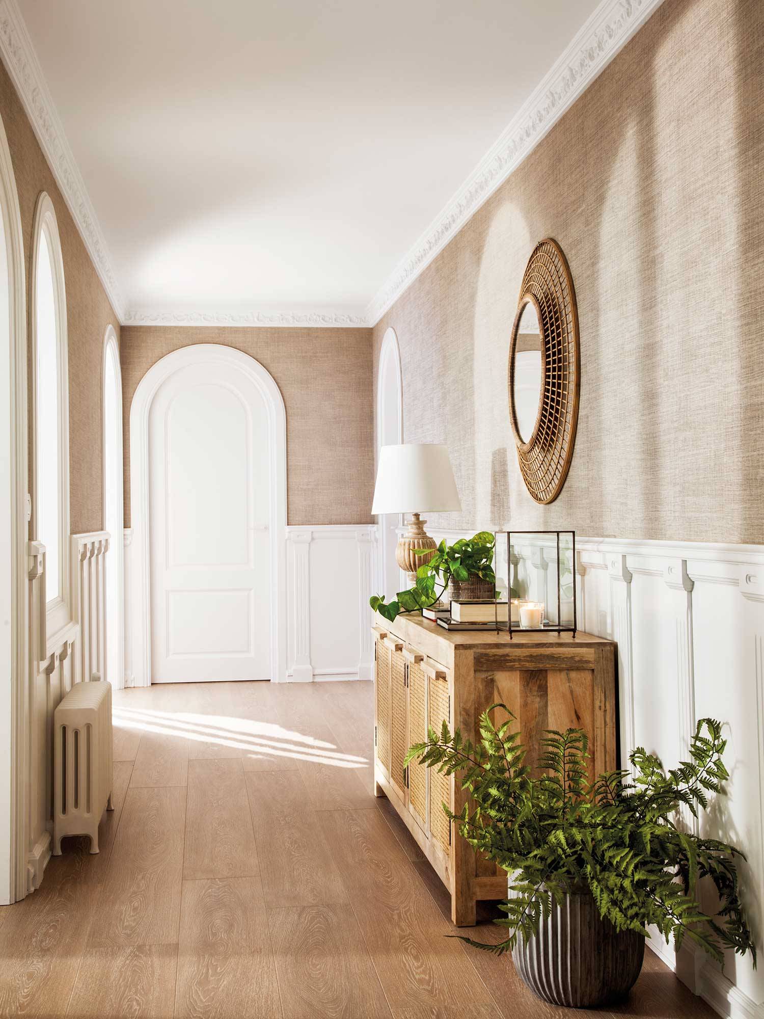 Recibidor clásico con aparador de madera, espejo redondo y paredes con molduras blancas.