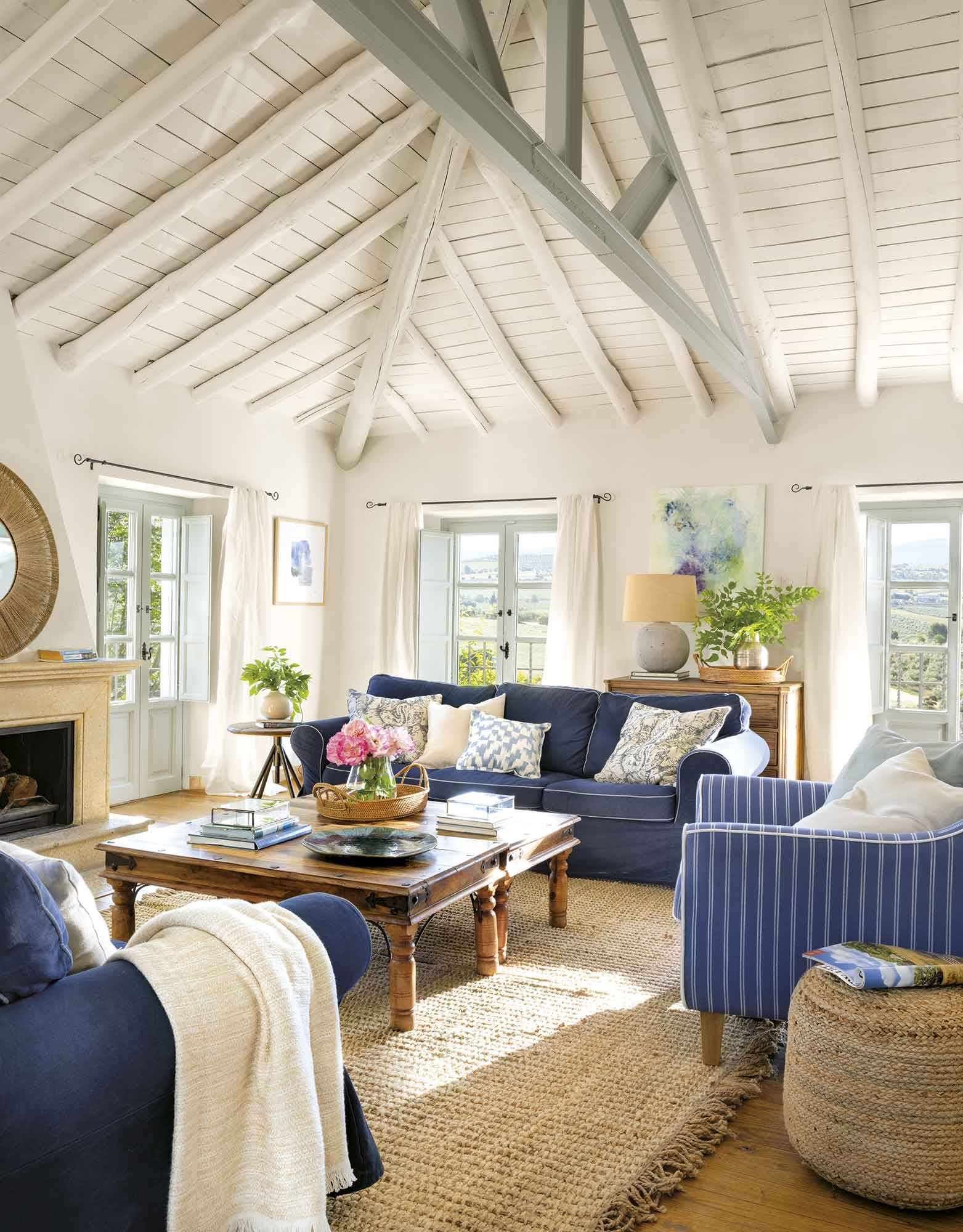 Salón con techos abuhardillados y sofás en azul. 