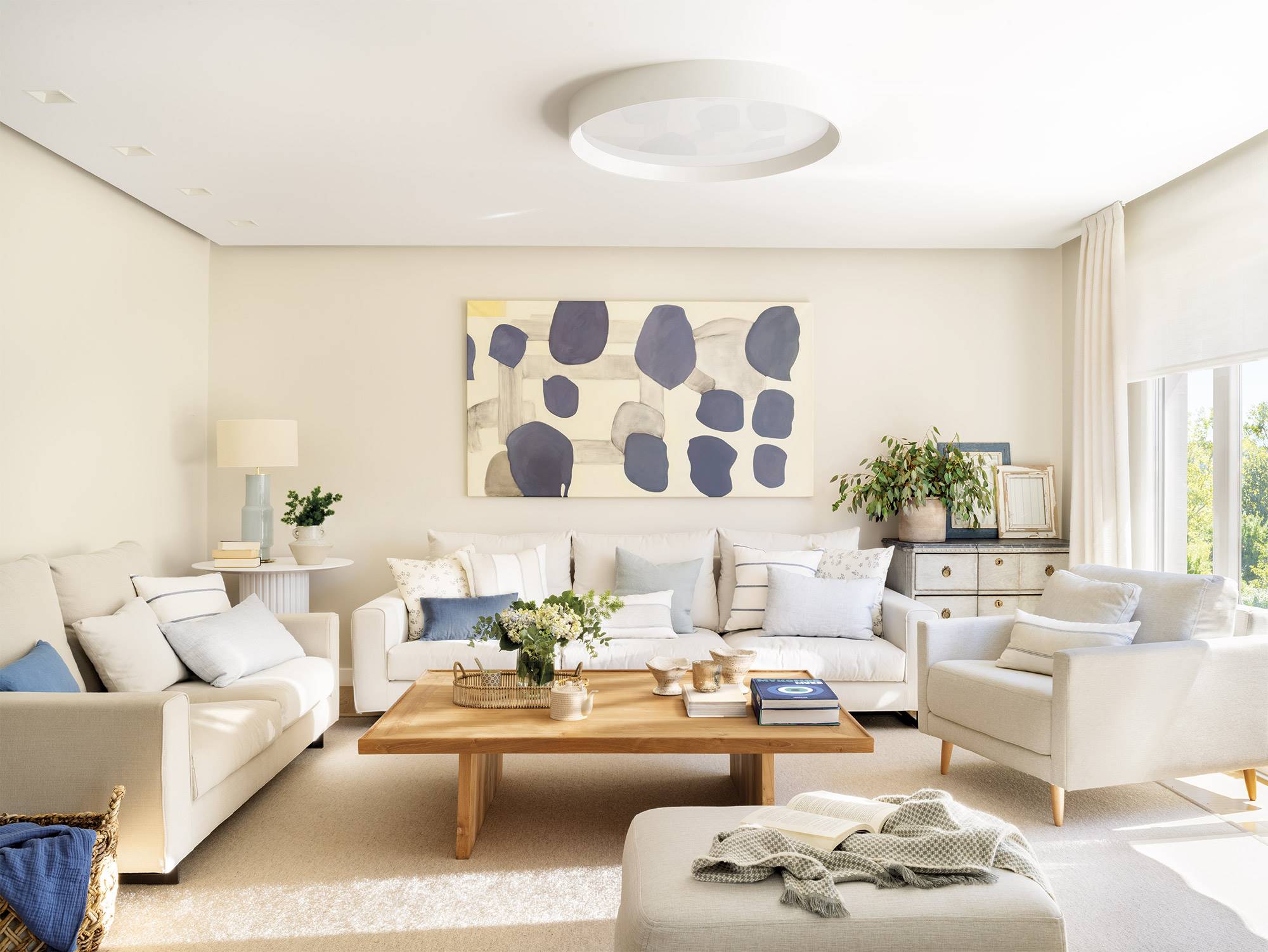 Salón con paredes y sofás en blanco roto, mesa de centro de madera y cojines en tonos azules. 